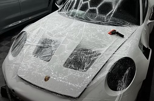 White Porsche car covered in ceramic and soap and water with a squeegee on top, in a garage or parking lot.