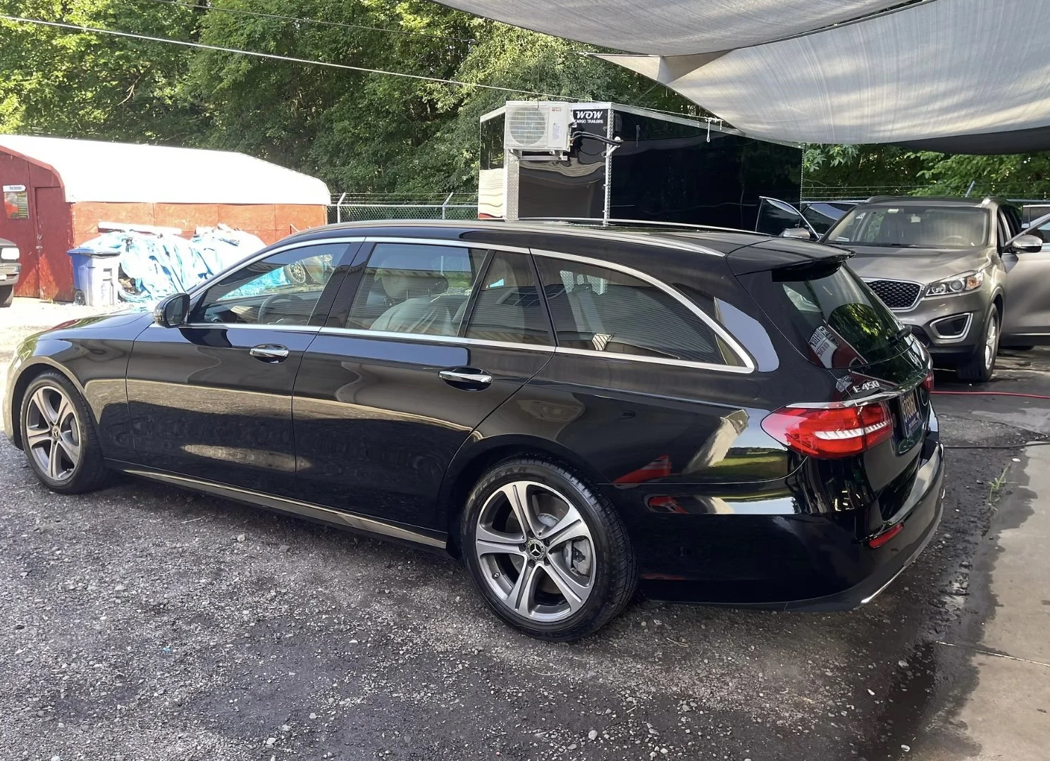 Black Mercedes-Benz E-Class station wagon parked outdoors on a gravel lot, with other vehicles and trees in the background.