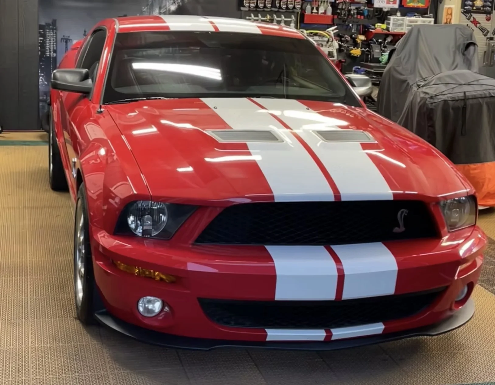 Red Mustang with white racing stripes inside a garage or workshop.