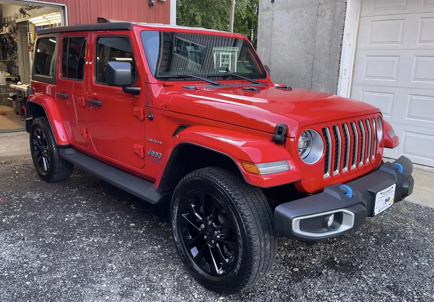 Red Jeep Wrangler parked outside, with black wheels and a black soft top, in front of a garage.