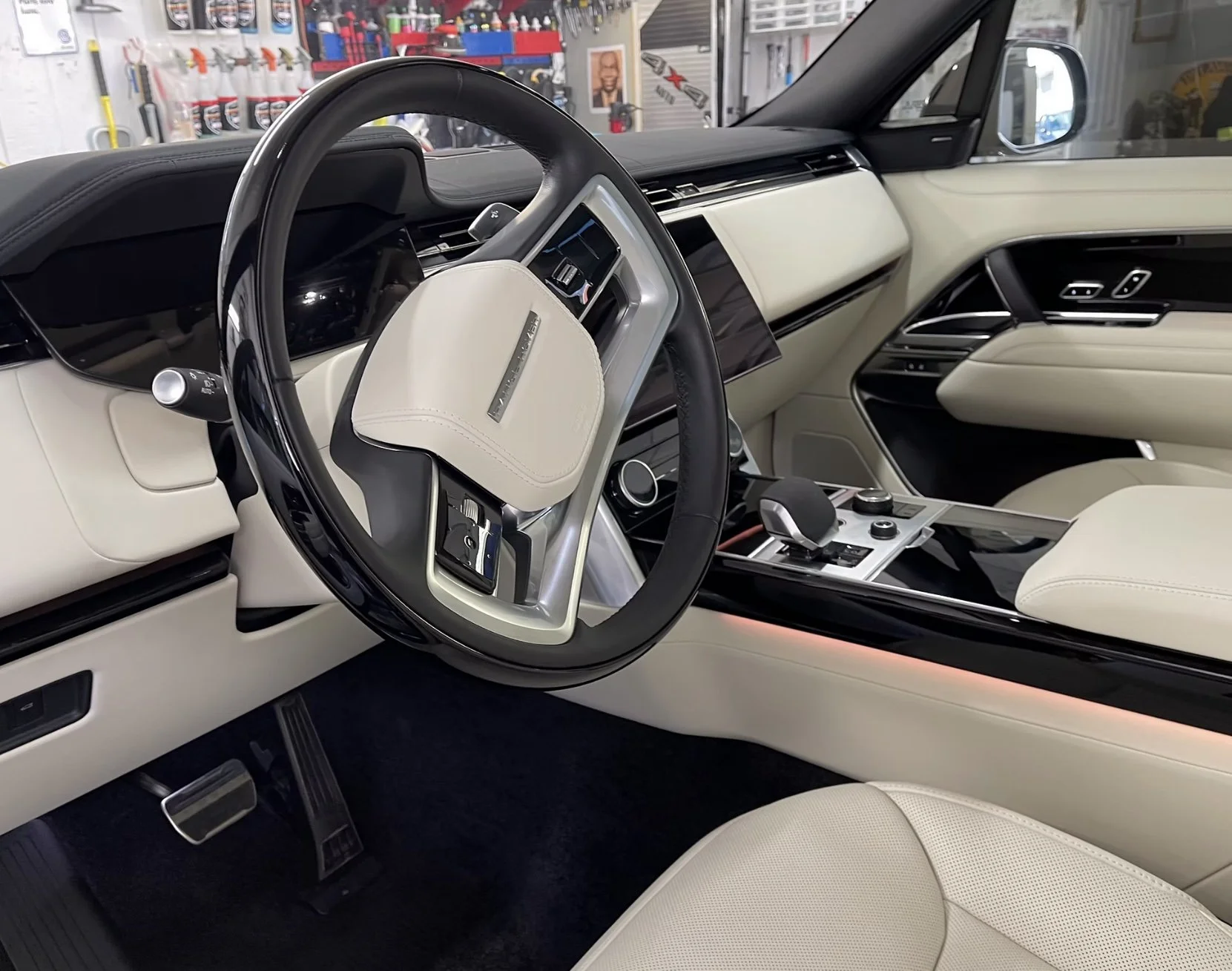 Inside the interior of a luxury car with a black and white color scheme. The steering wheel features a logo, and the dashboard has digital displays and controls. The center console holds various buttons and dials, and the seats are upholstered in cre