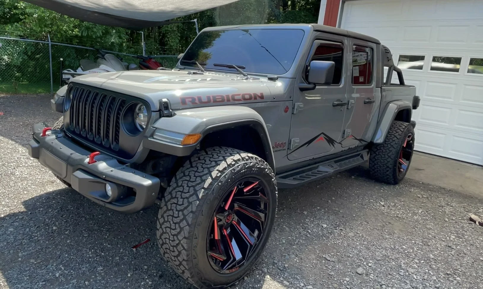 Gray Jeep Rubicon parked in driveway with large off-road tires and custom black and red rims