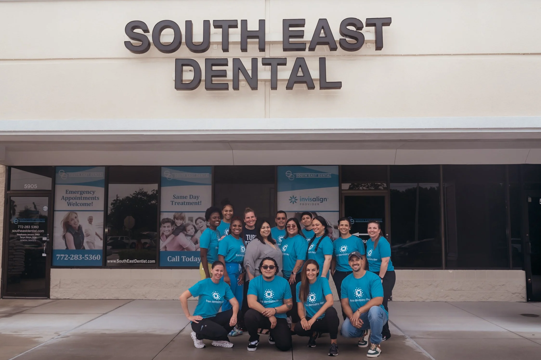Group of smiling dental team members in matching blue shirts posing outside South East Dental clinic.