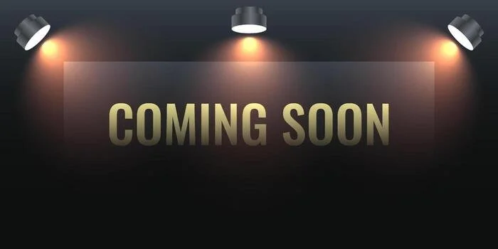 A dark wall with a lighted sign that says 'COMING SOON' in bold, yellowish letters, illuminated by three ceiling lights.