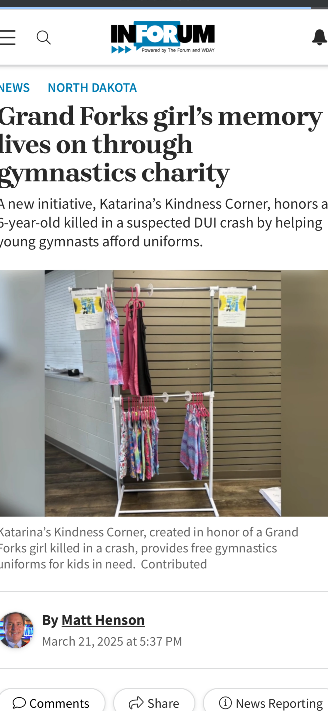 A display of colorful gymnastic uniforms on a clothing rack in a community center or gym. The uniforms are pink, blue, and multi-colored, used for a charitable event. The background has a wooden slat wall and partial view of a window.