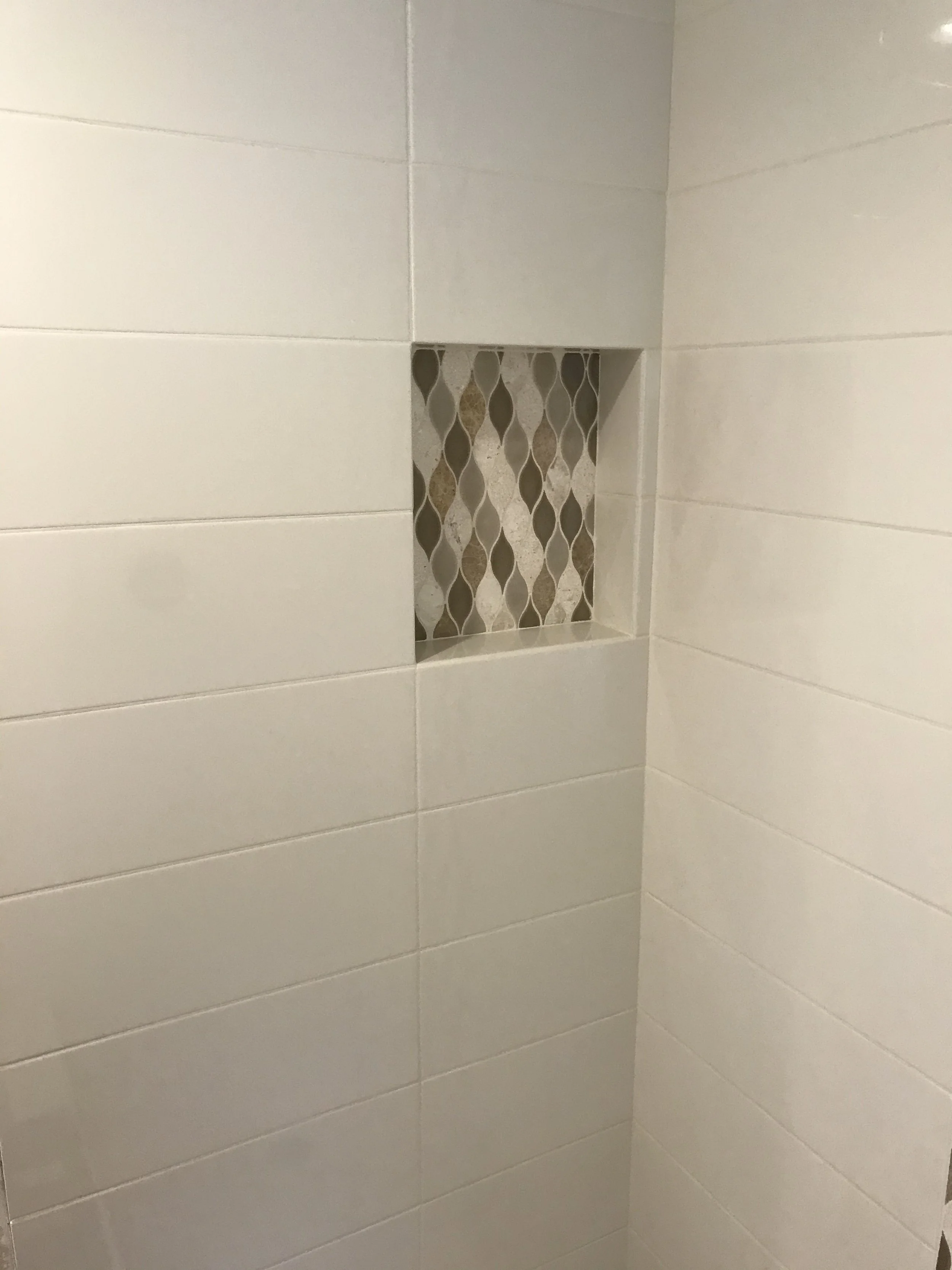 A bathroom wall with three white tiles and a recessed niche containing decorative beige and brown diamond-patterned tiles.