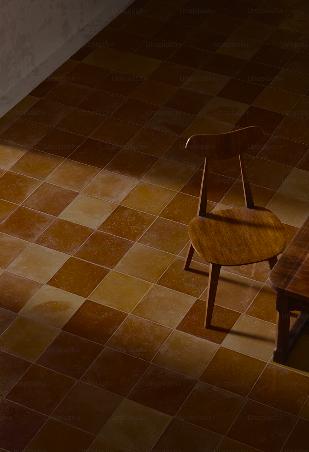 A wooden chair with a curved backrest and four legs is situated on a tiled floor with brown and tan squares. A wooden table is partially visible on the right side of the image. The scene is softly lit.