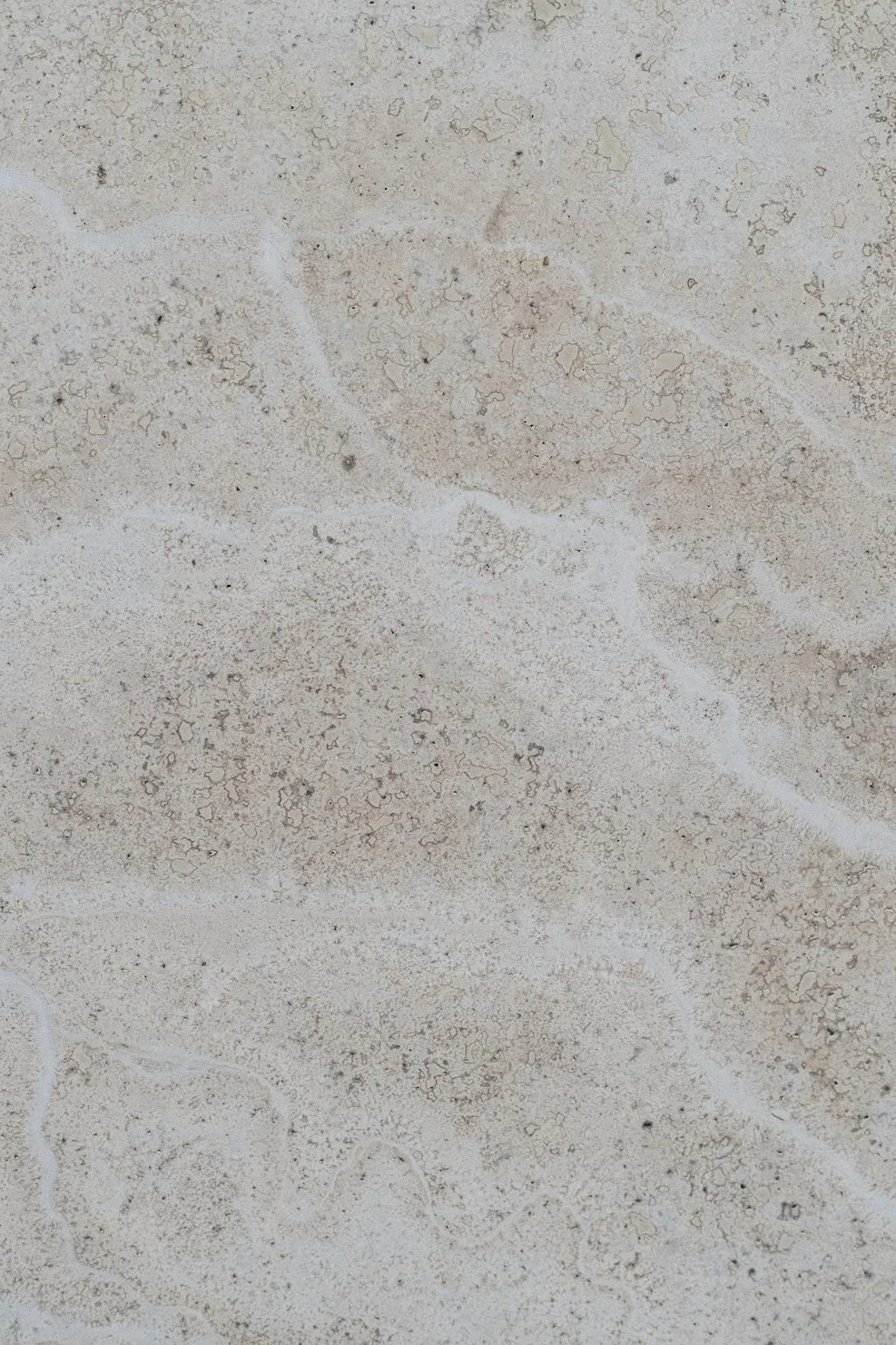 Close-up of a textured, light-colored stone or concrete surface with natural cracks and patterns.