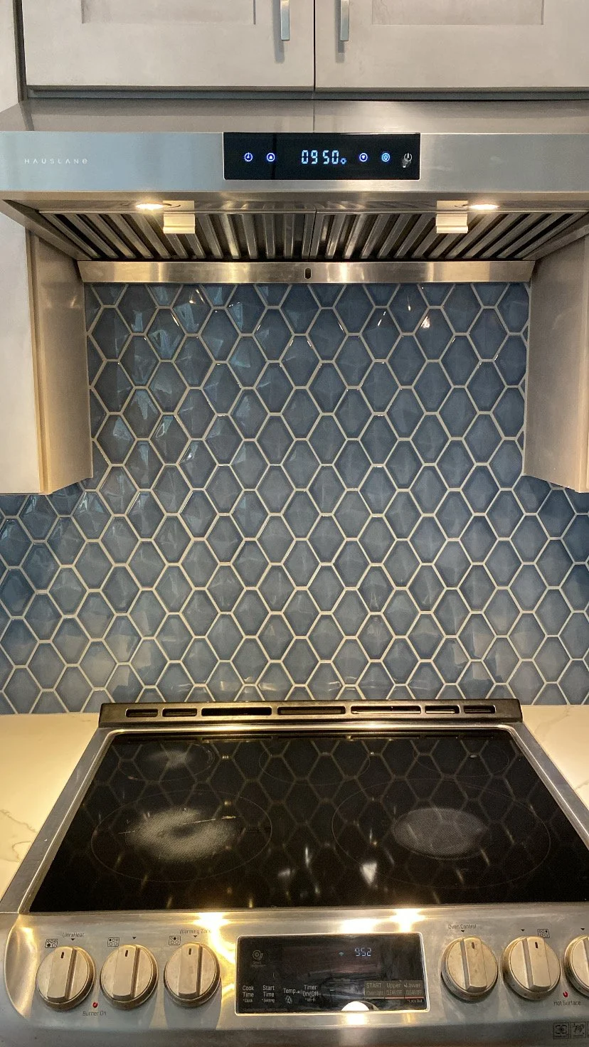 Kitchen with stovetop and hexagonal tile backsplash, digital clock on range showing 9:50, and modern cabinetry.