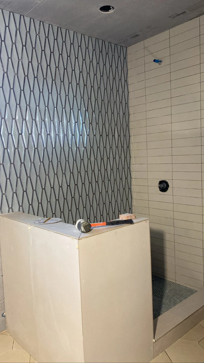 Interior of a bathroom under construction with tiled walls, a partially installed shower area, and tools on a counter.