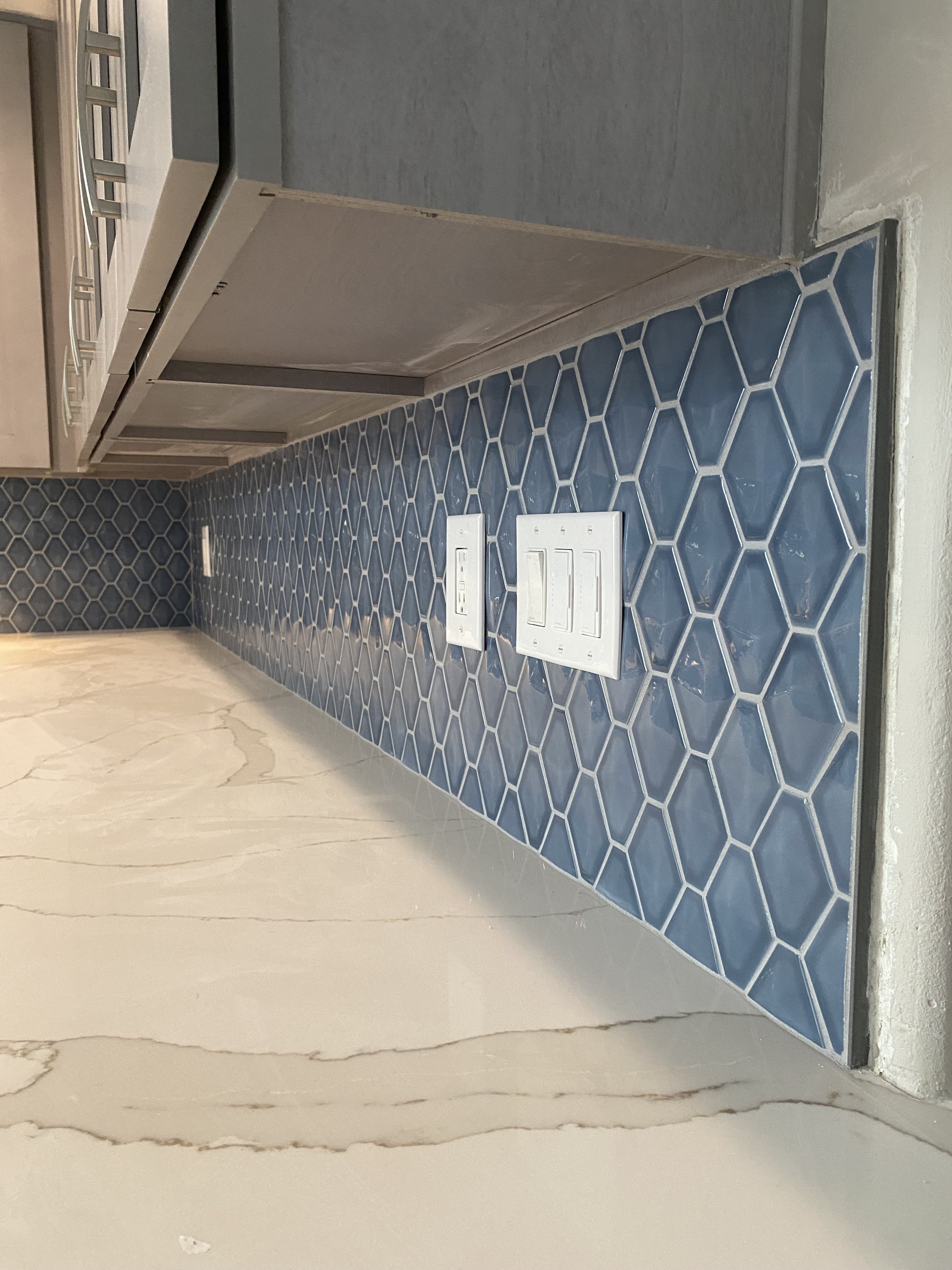 Close-up view of a kitchen countertop with blue hexagonal patterned tiles, electrical outlets, and a section of the stove.