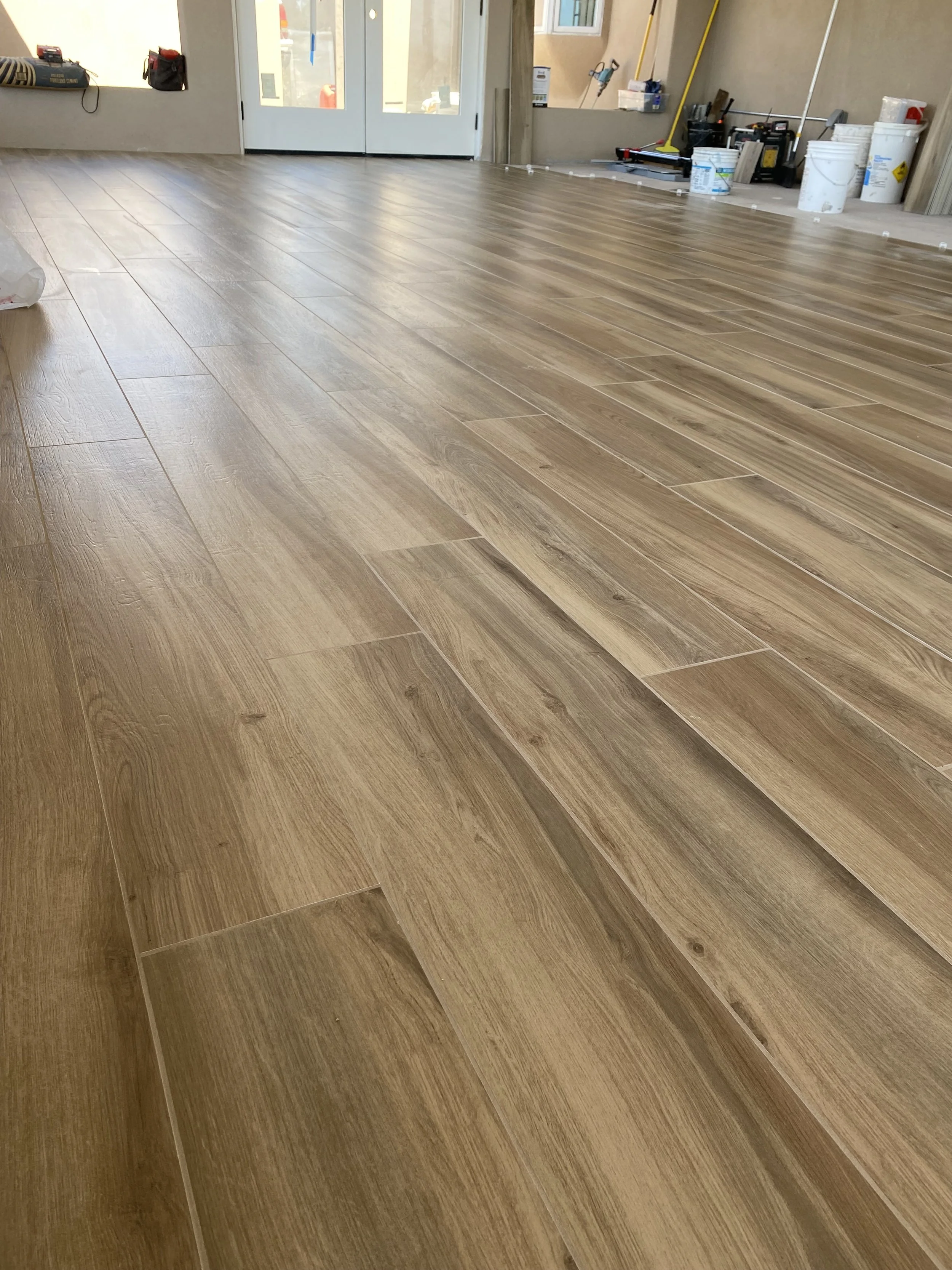 Newly installed wooden floor tiles in a room with construction tools and supplies visible in the background.