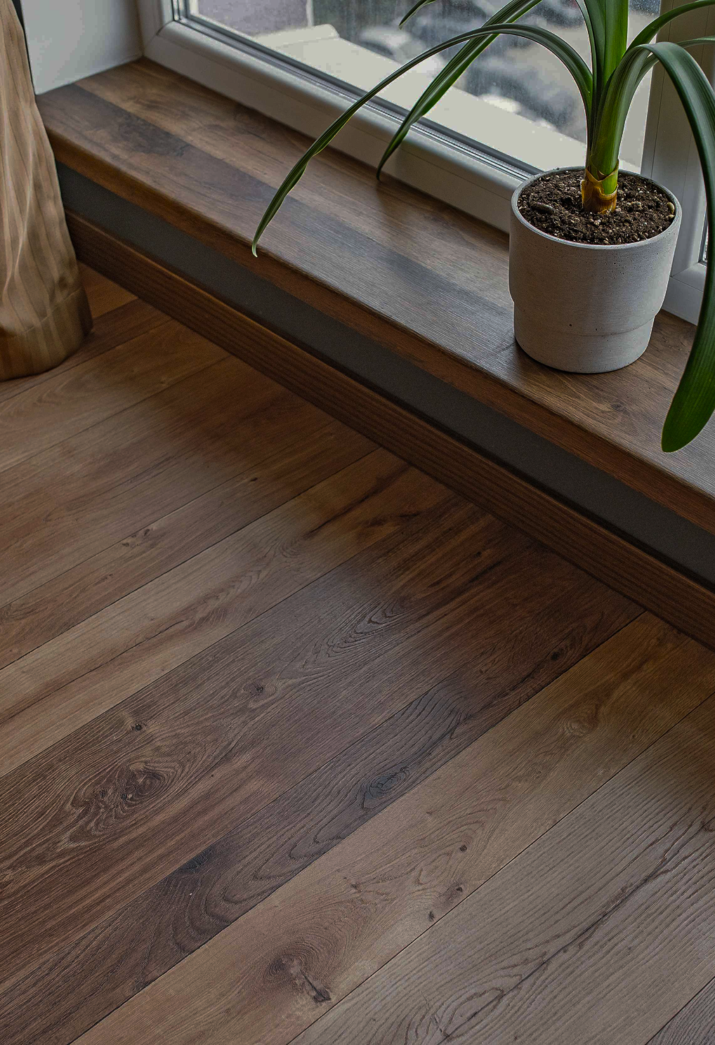 Wooden windowsill with a potted plant near a window, showing hardwood floor with wood grain patterns.