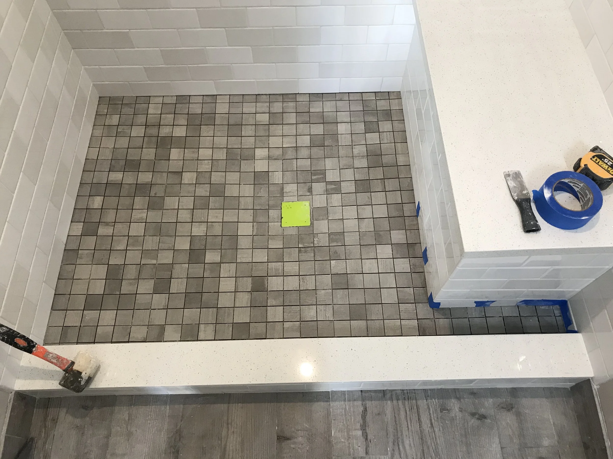 Bathroom with white subway tile walls, a tiled shower base, and a white countertop with tools and tape on it, indicating ongoing construction or renovation.