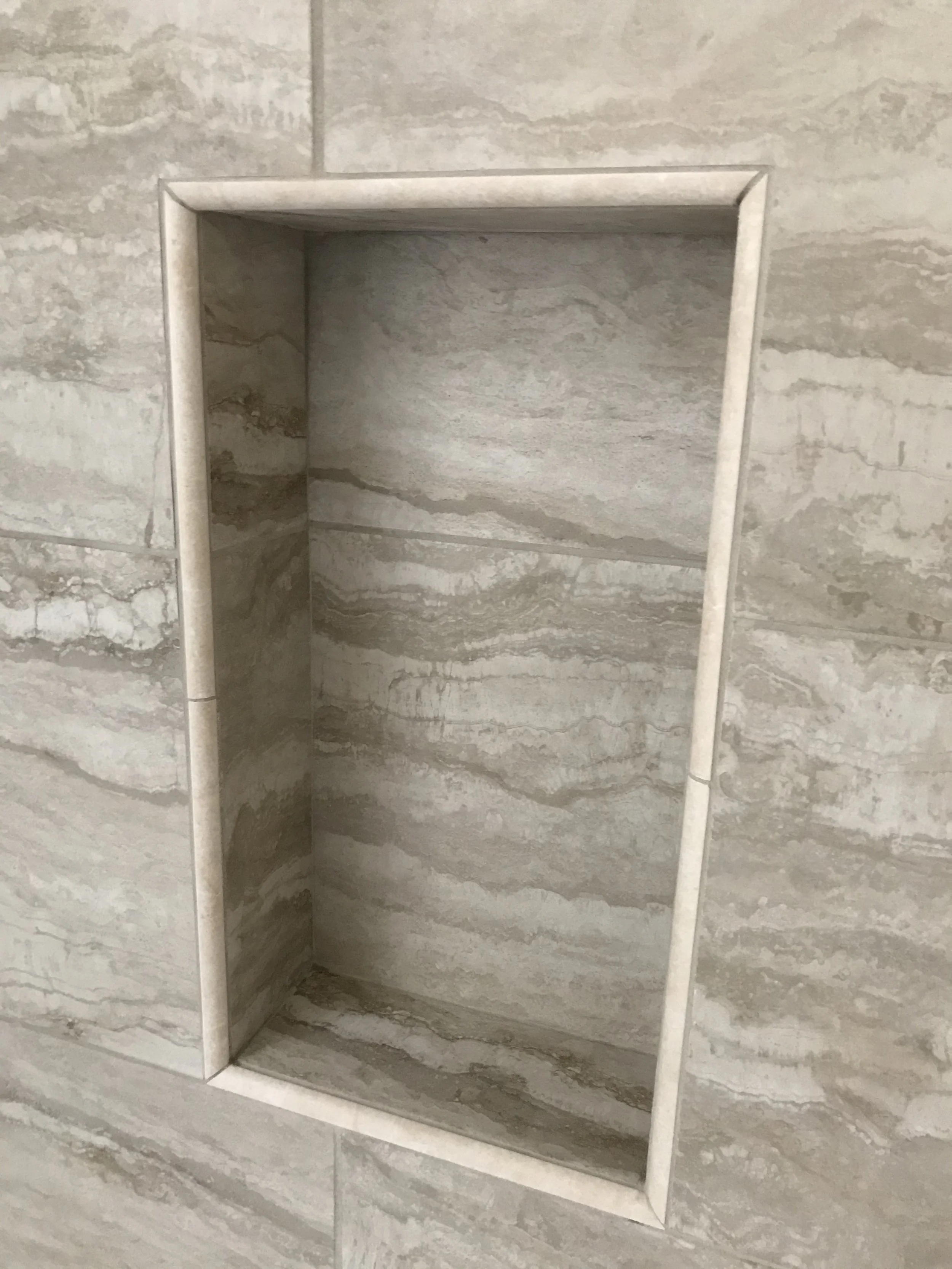 Recessed shower or niche with marble tiles on walls, built into a marble-tiled wall.