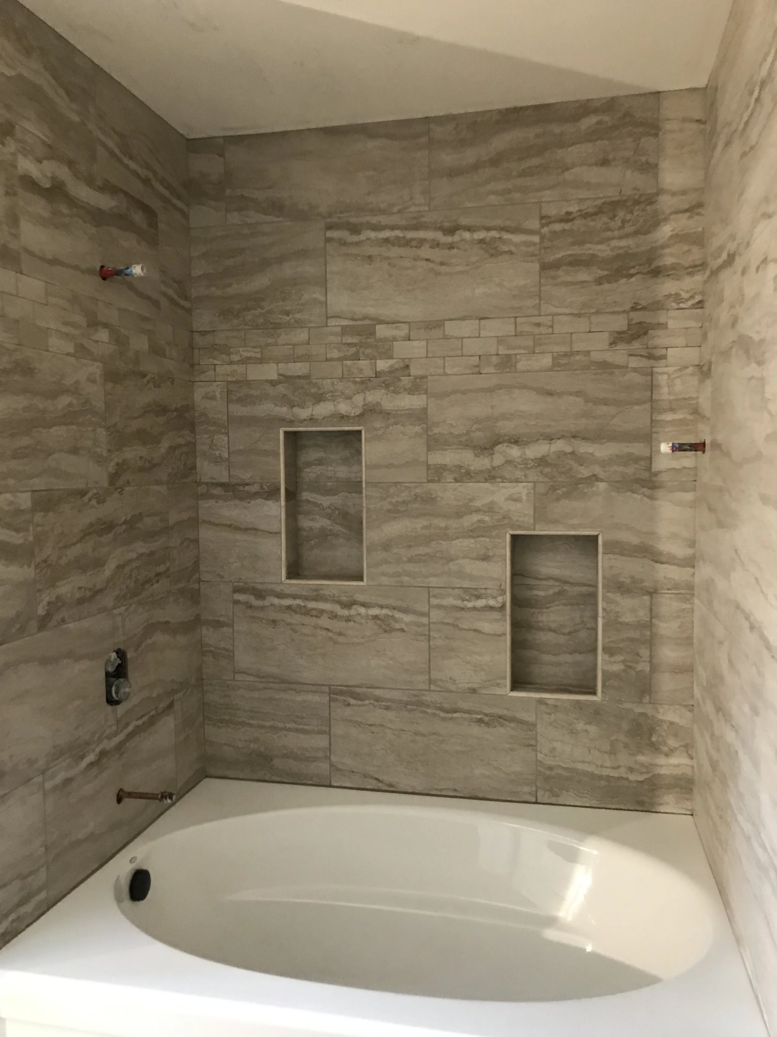Bathroom shower with beige marble tiles, built-in niches, and plumbing fixtures.