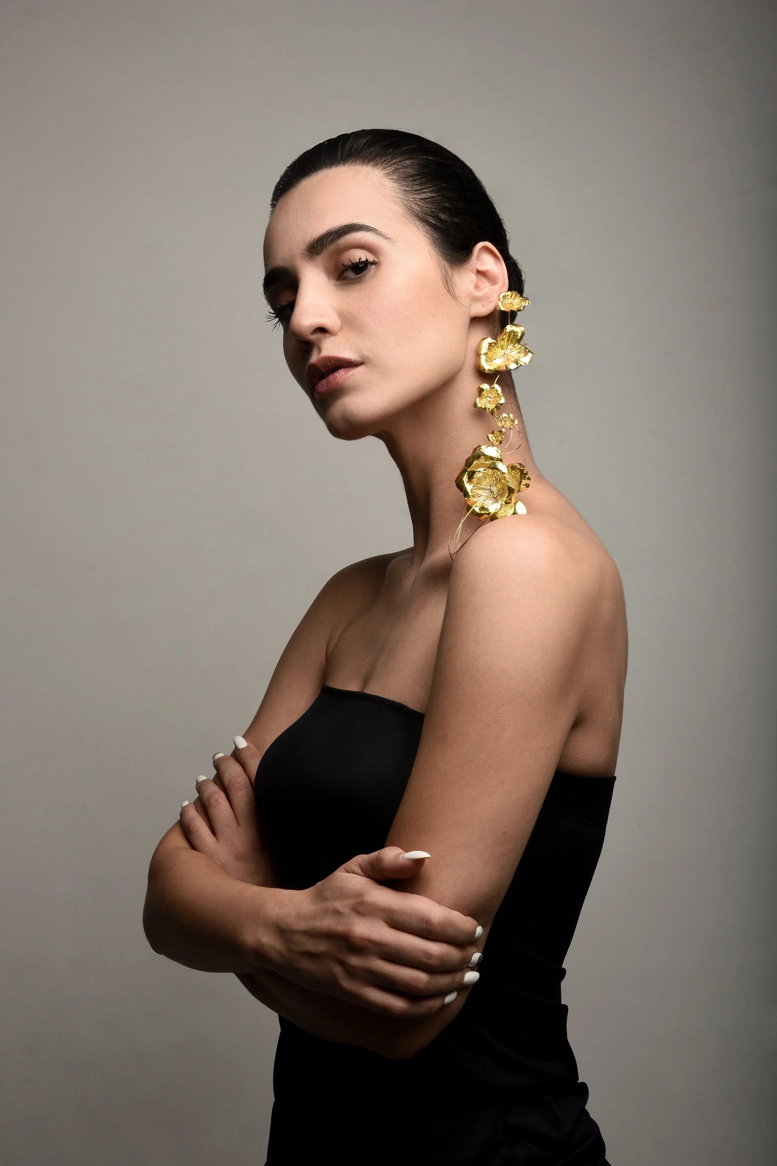 A woman with dark hair tied back, wearing a strapless black top, and large gold floral earrings.