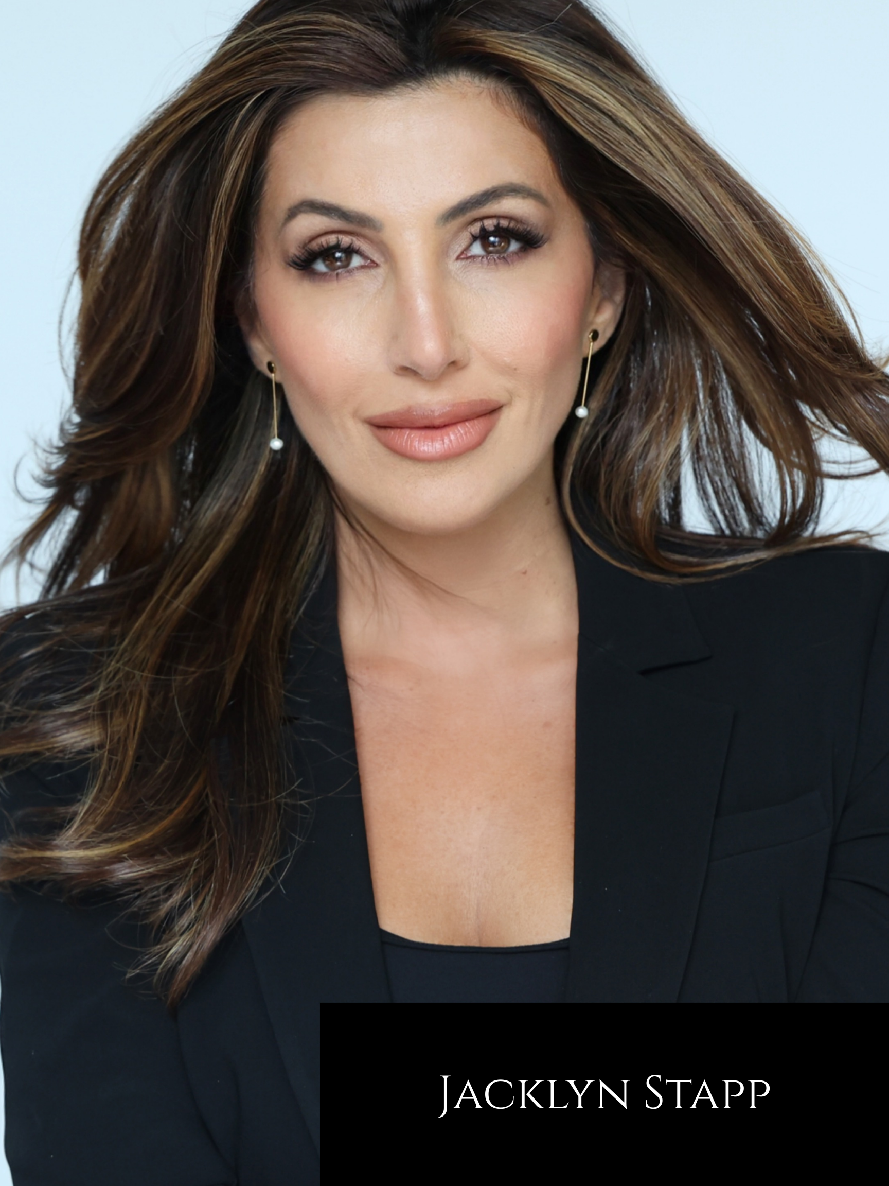 A woman with long, wavy brown hair and earrings, wearing a black blazer, looking at the camera. Text overlay displaying "Jacklyn Stapp".