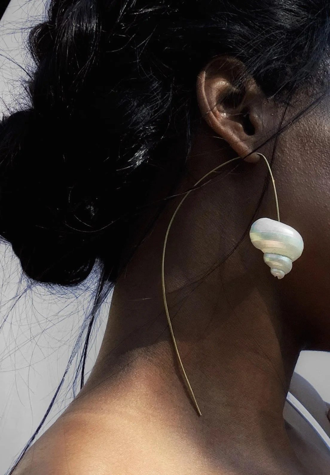 Close-up of a person with dark skin and braided hair, wearing large shell earrings and a necklace with a shell pendant.