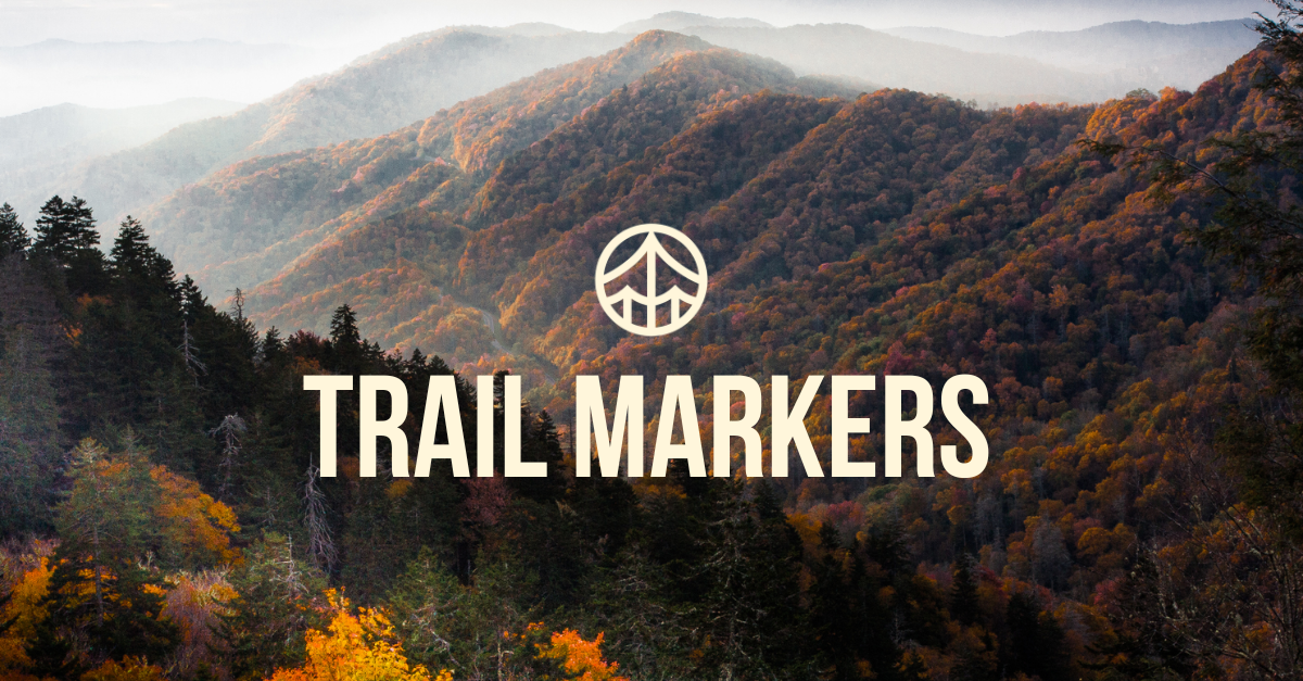 A scenic view of a mountain range with autumn-colored trees in the foreground and misty peaks in the background, with the words "Trail Markers" and a trail icon in the center.