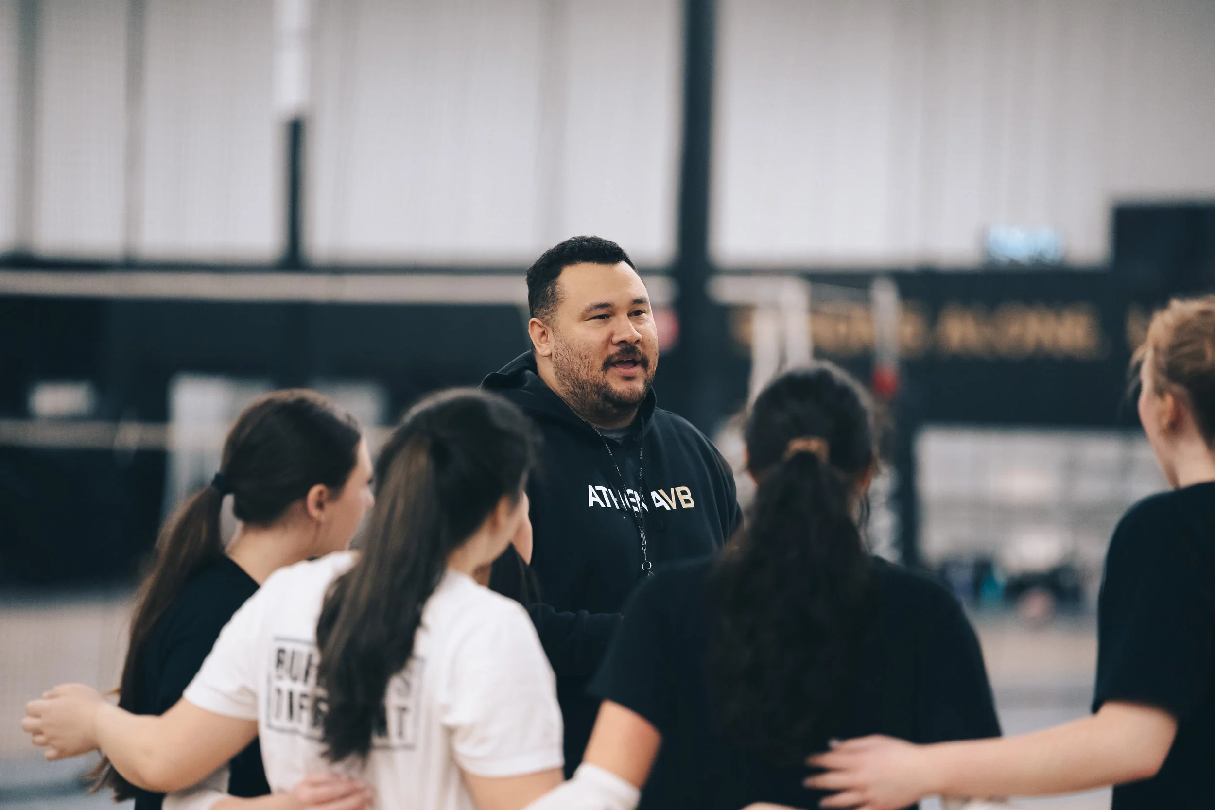 A volleyball coach named coachk808 leading a team meeting with four women volleyball players in a gym or sports facility.