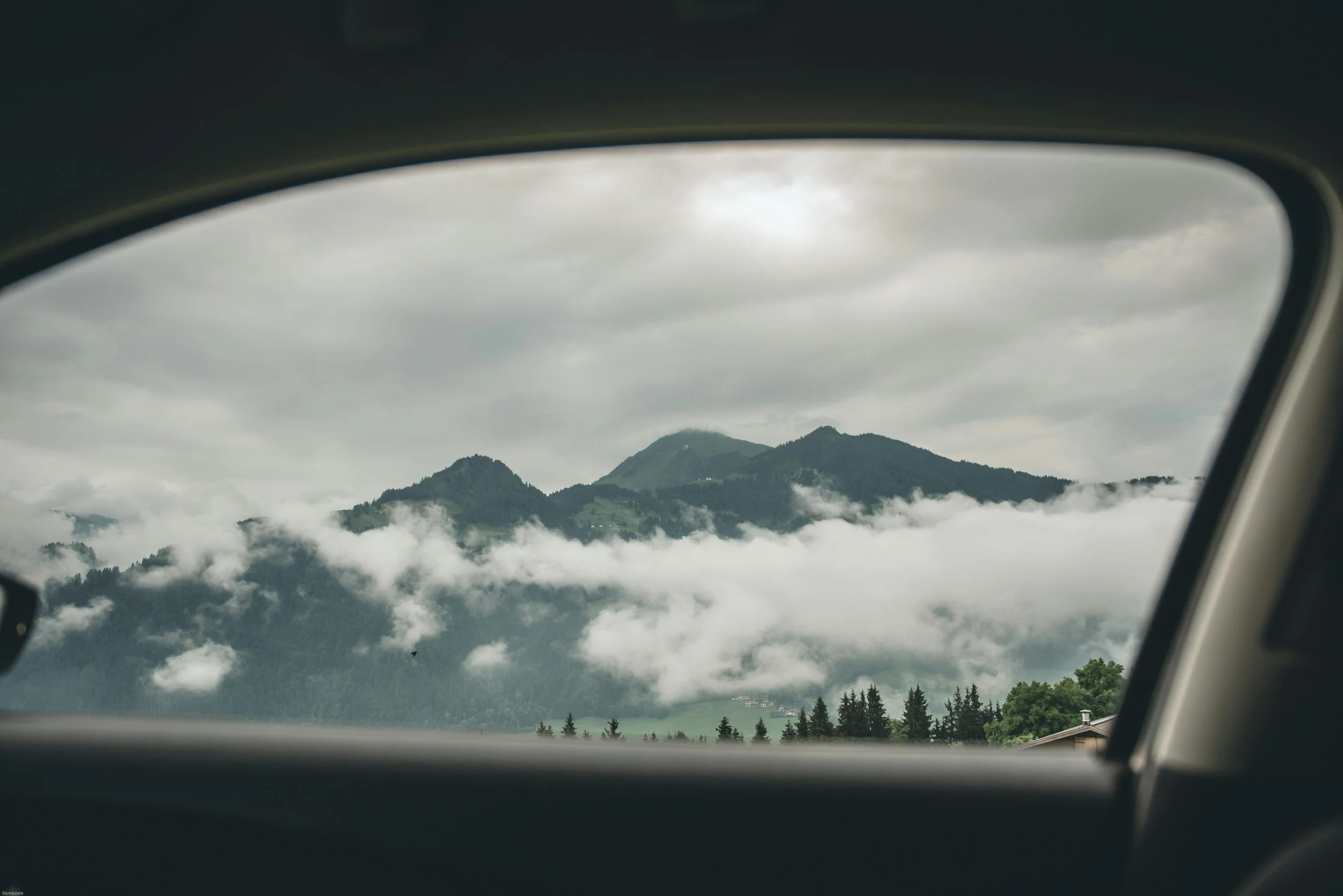Mountain landscape seen through the car window with fog and clouds in the sky.