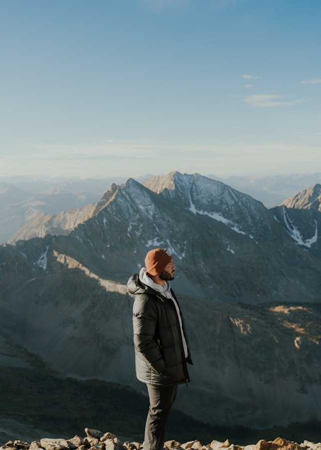Person standing on a rocky ridge facing an expansive mountain range, creating a sense of scale and openness.