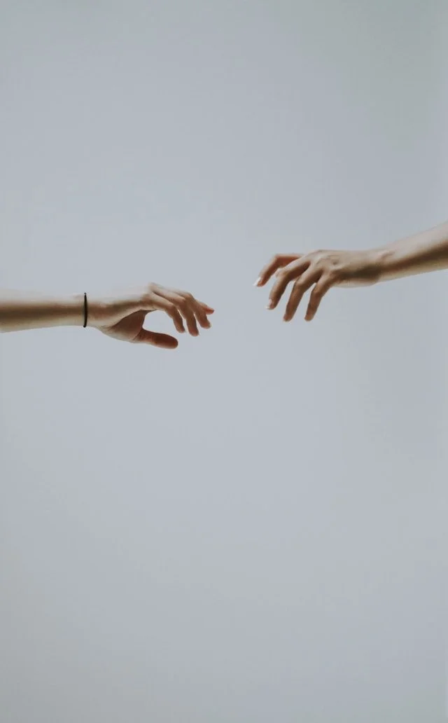 Two hands reaching toward each other with fingertips almost meeting, suggesting connection and support.