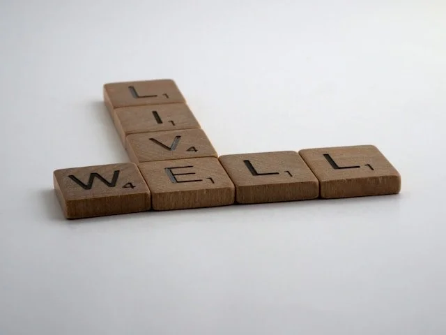 Scrabble tiles forming the words ‘LIVE’ and ‘WELL’ in a simple crossword arrangement, creating a calm, encouraging message.