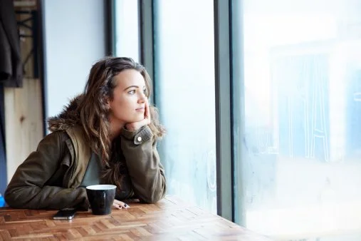 Girl contemplating as she looks through a window.