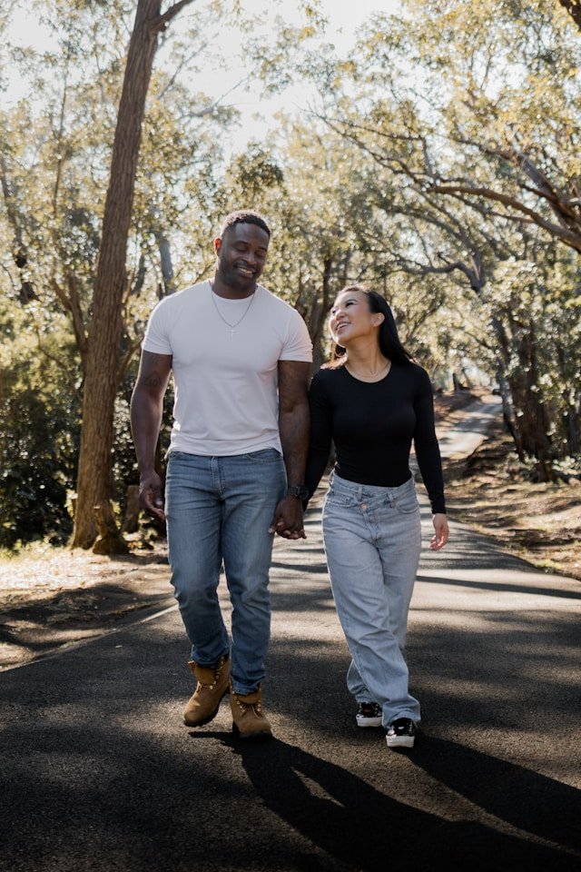 A pair walks together down a wooded trail, staying close as they follow the winding path beneath the afternoon light.