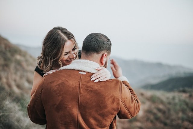 Two people sharing a quiet, supportive moment on a hillside overlooking soft, misty mountains.