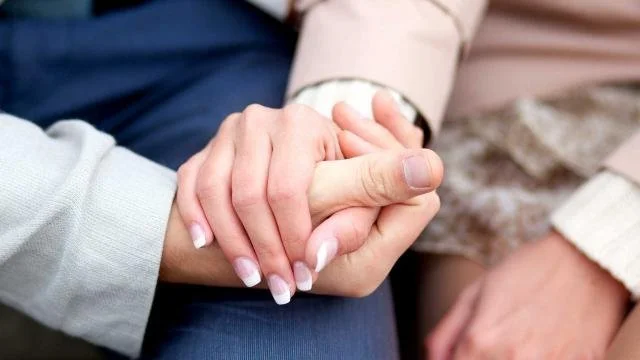 A couple holding hands with their hands in their lap.