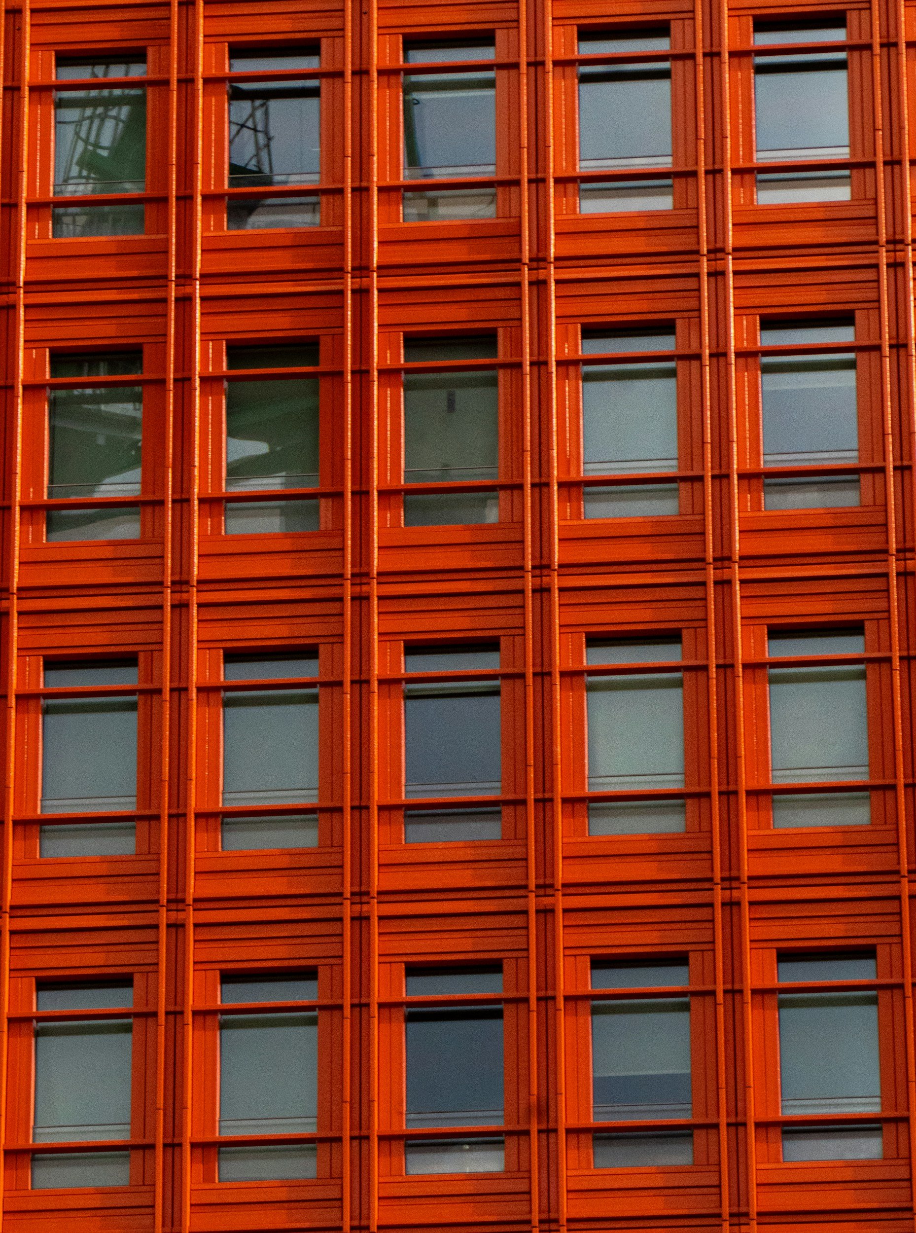 Close-up of a building's exterior with a pattern of red-orange wooden or metal panels and large glass windows.