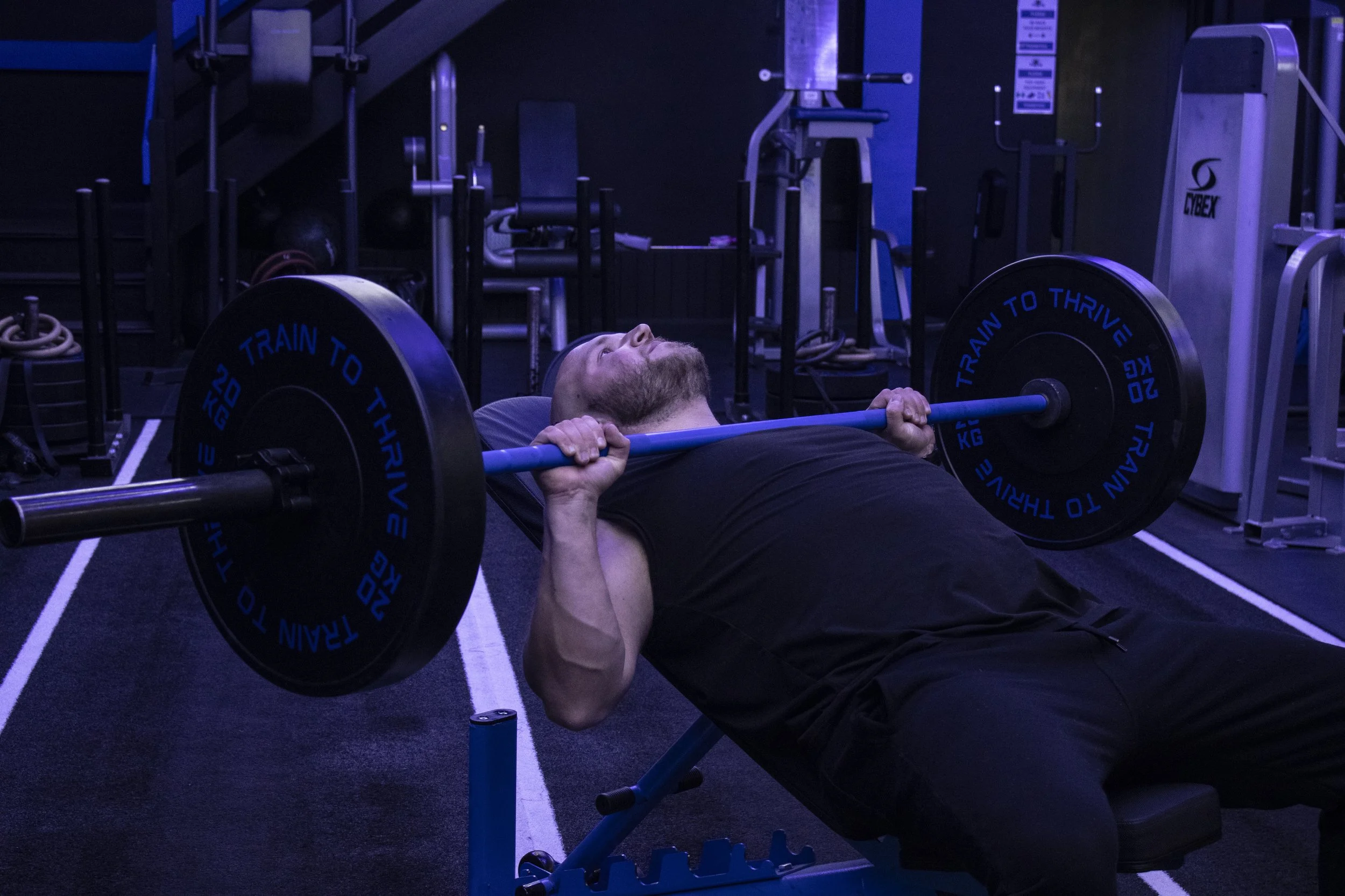A man doing high incline bench press at a gym, pressing 60 kilo grams for repetition in a black vest, at a gym in Carlisle, Cumbria.