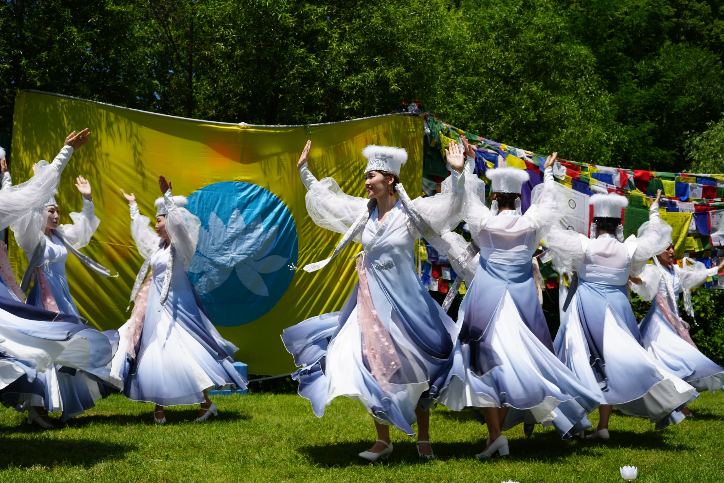 Women in traditional Korean hanbok performing a dance outdoors with a large yellow flag featuring the blue and white emblem of the United Nations in the background.