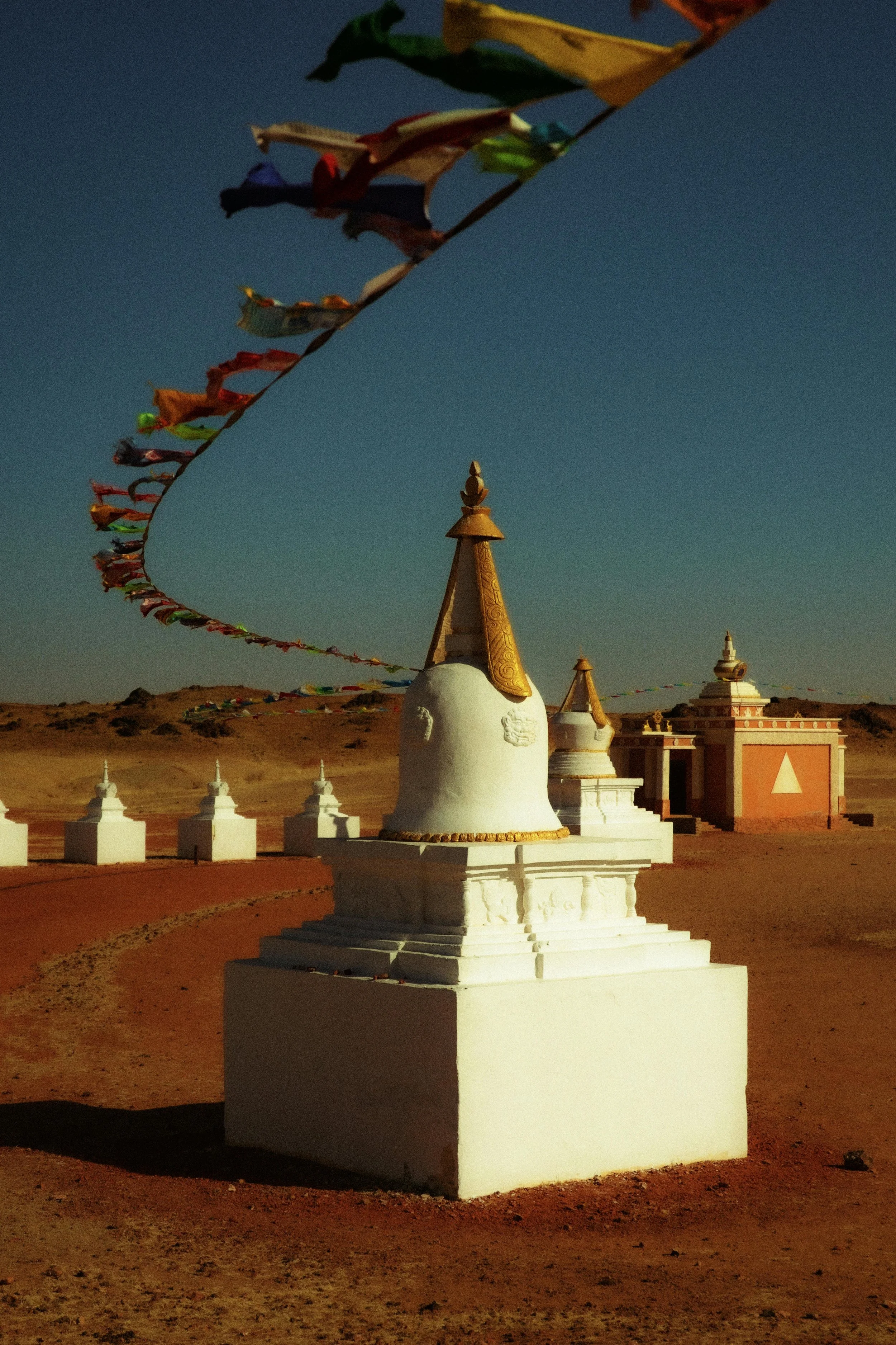 A desert landscape with white Buddhist stupas and prayer flags under a clear blue sky.