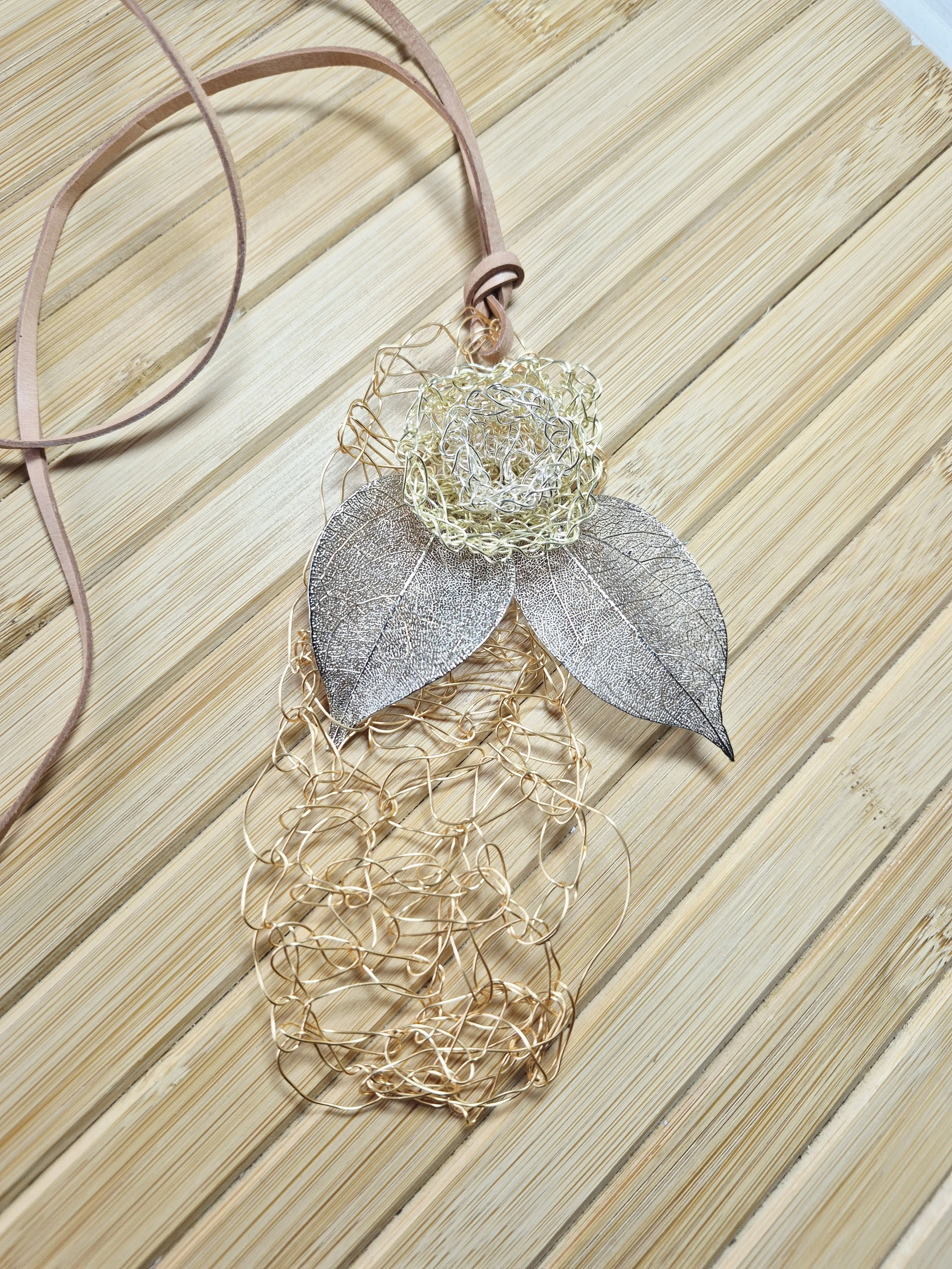 Decorative wire flower with metallic leaves on a wooden surface.