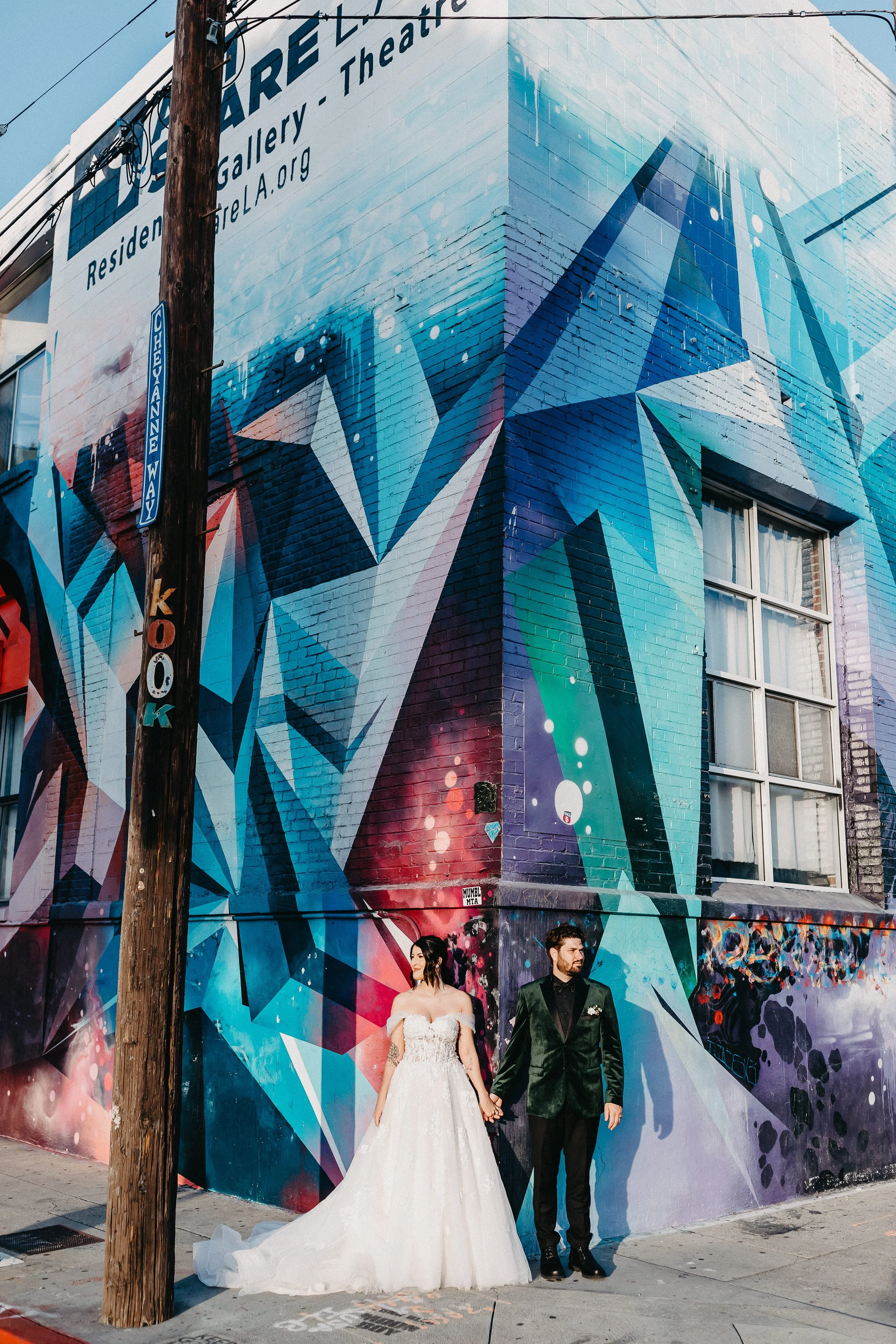 a couple in their wedding attire in downtown Los Angeles Art District up against a colorful painted wall.