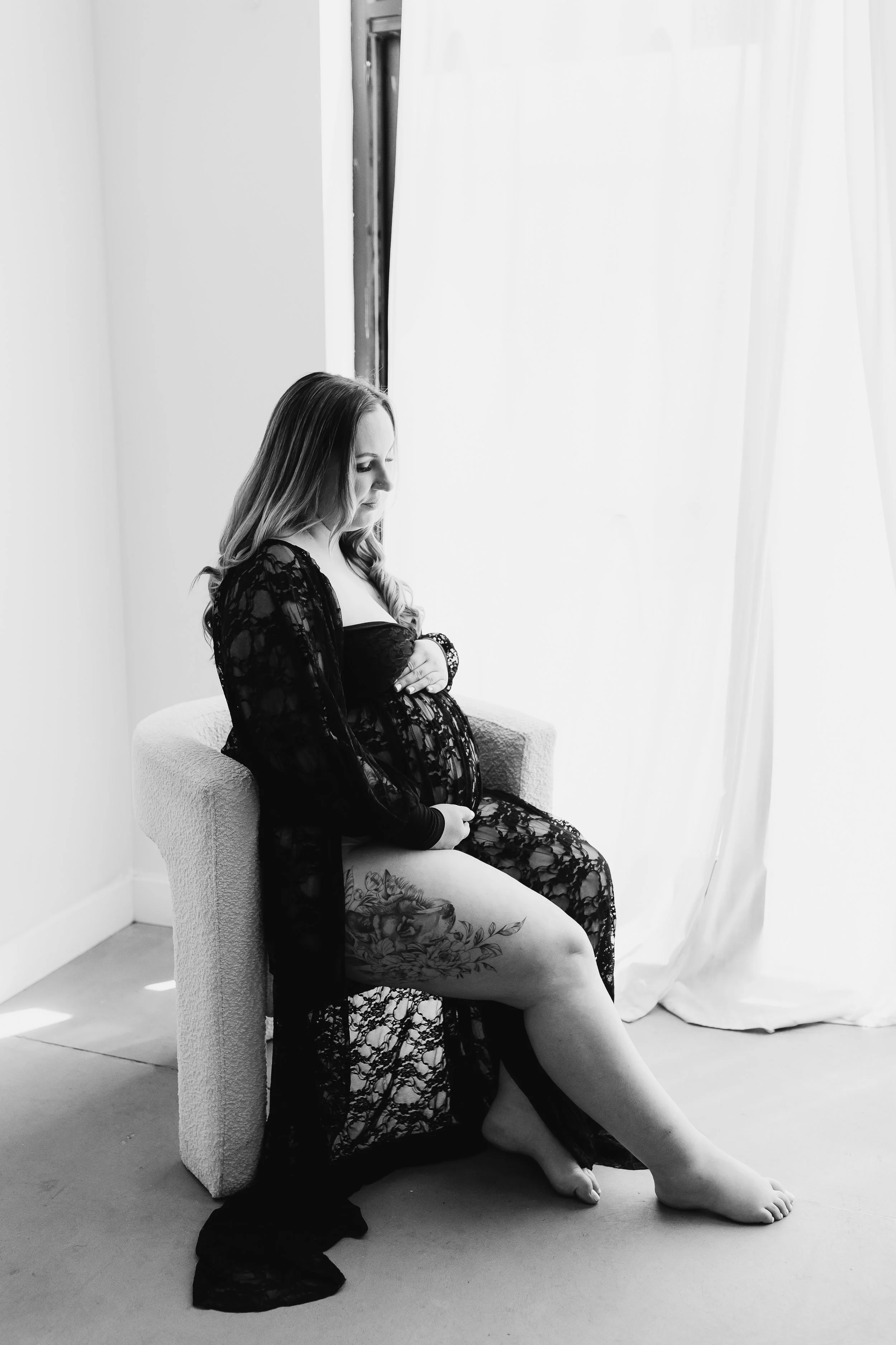 pregnant woman in floor length black robe and matching lace bodysuit sitting in chair