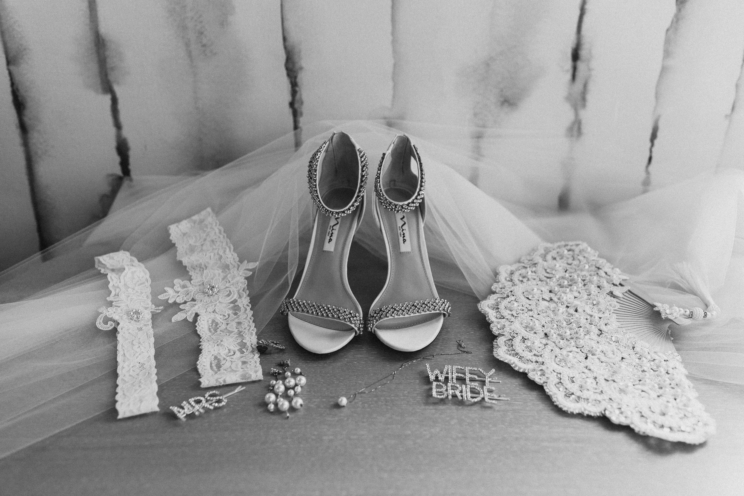 bridal props like heels, garters, earrings, fan, hair clips and necklace on table with floor length veil