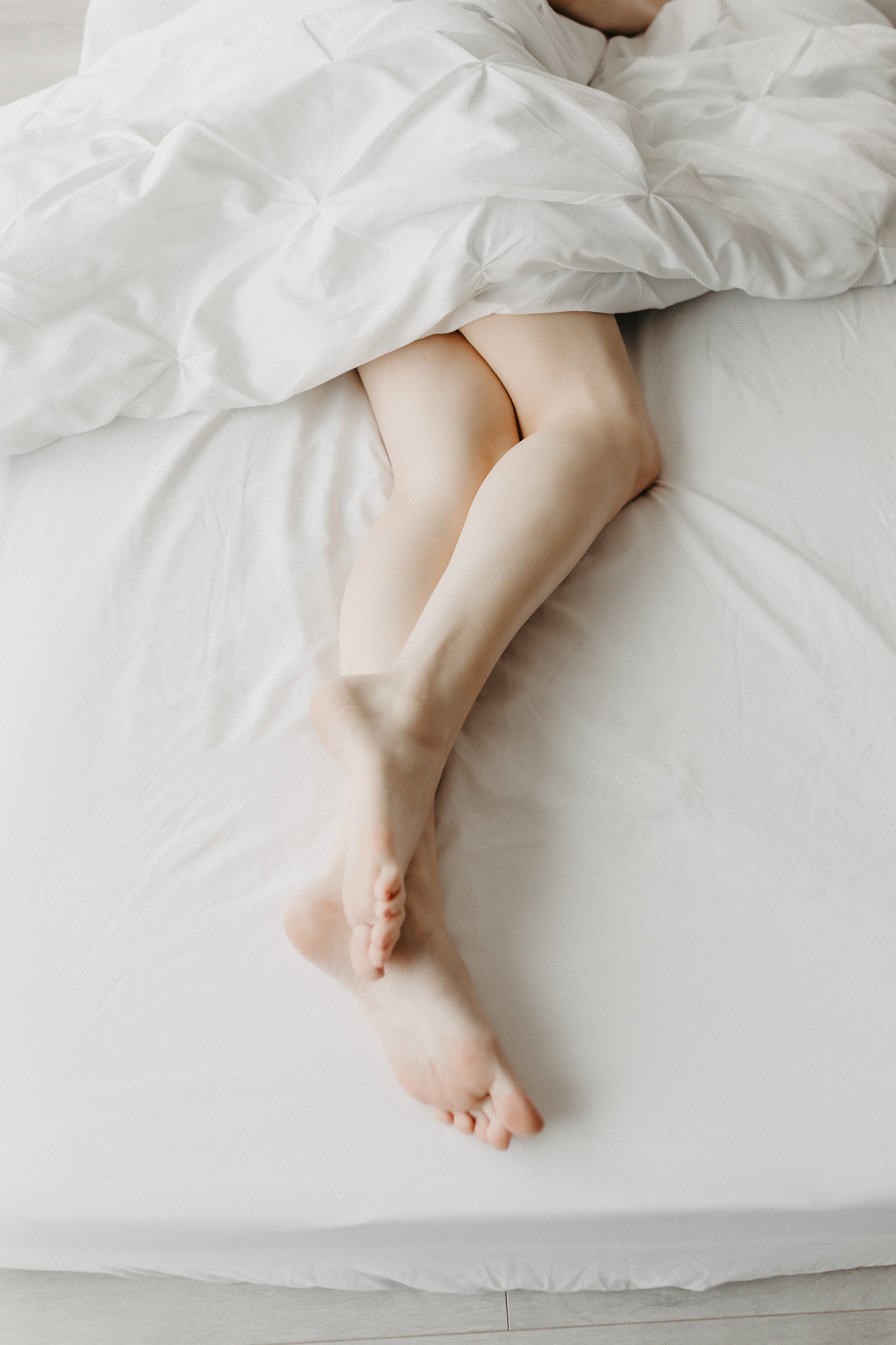 bride laying under white sheets with her bare legs showing