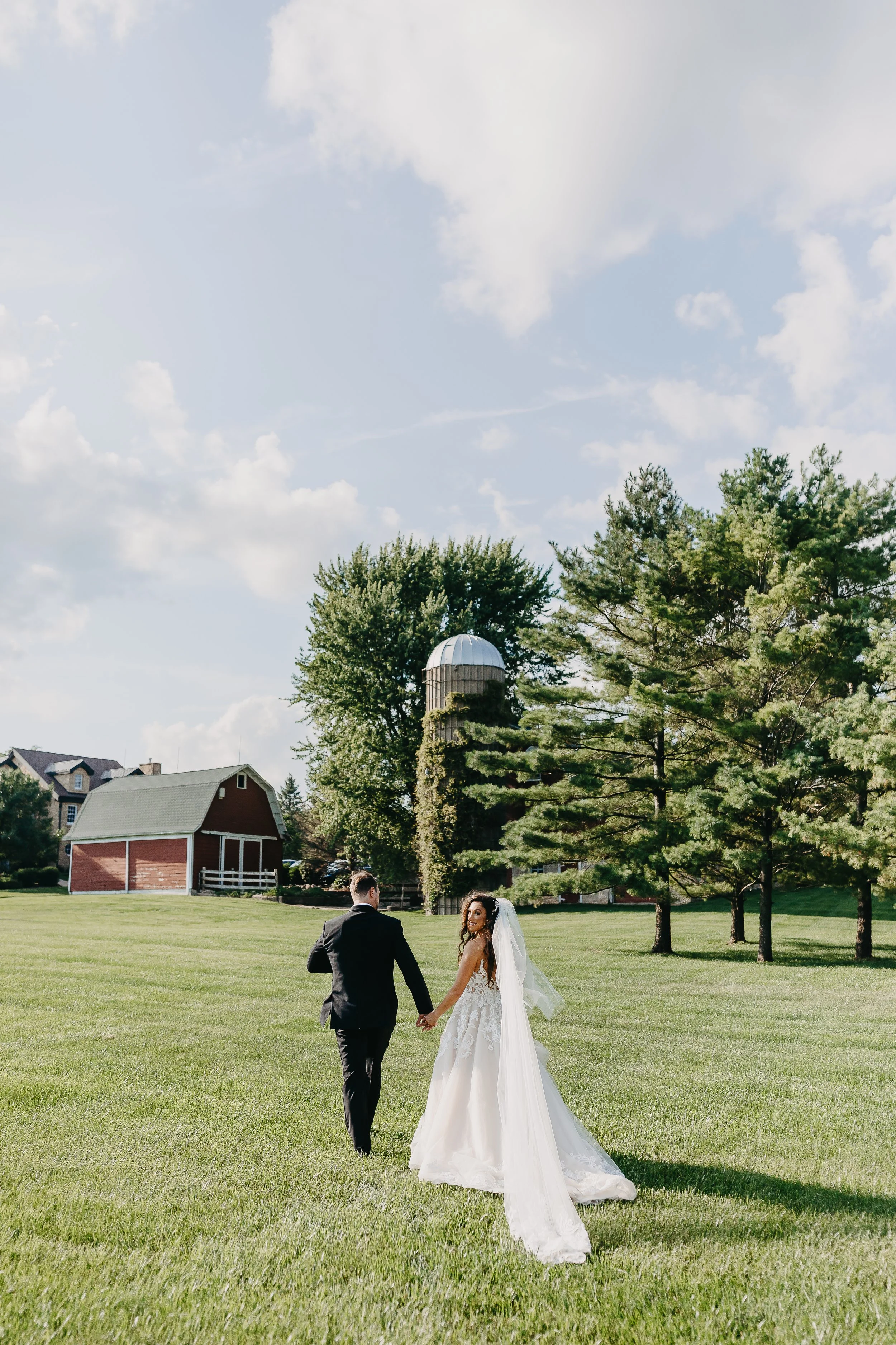 bride and groom walking away with the bride looking back at a farm wedding venue in Illinois.