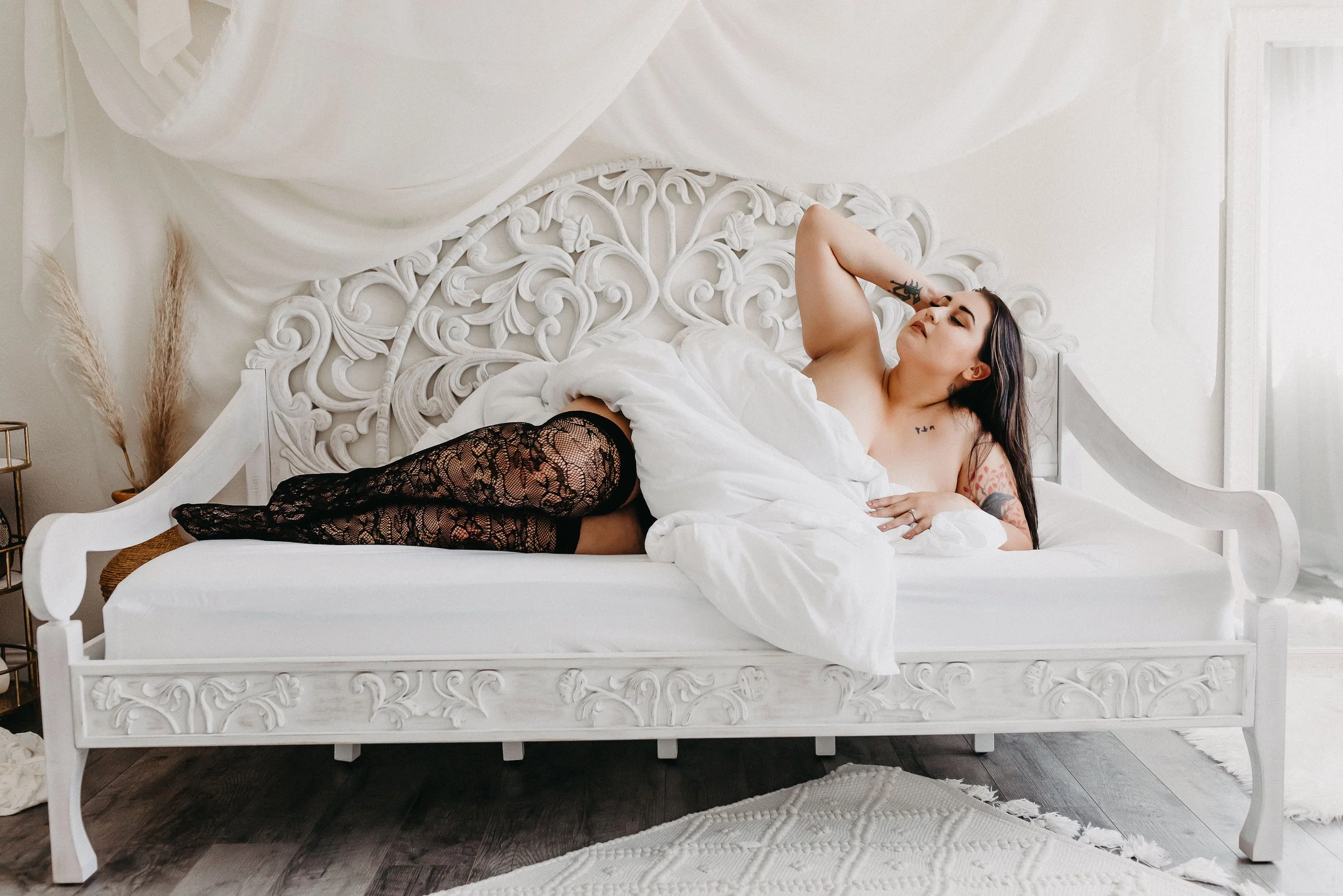 bride laying posed under the sheets on a vintage bed with black lace stockings