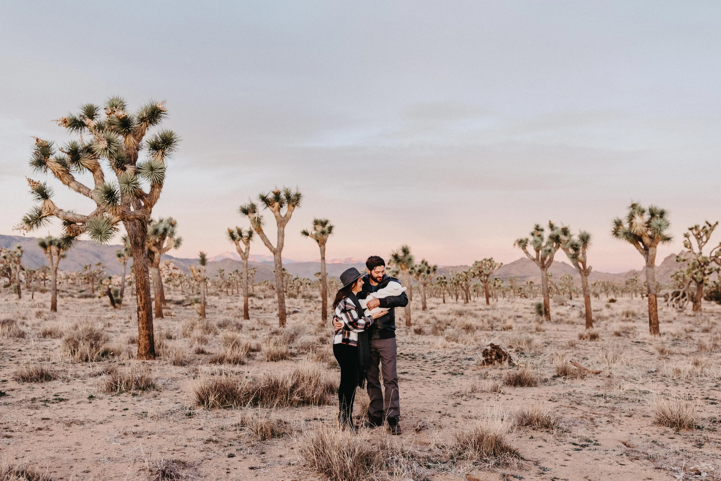a wife, her husband and their newborn baby at a sunrise session in Joshua Tree National Park