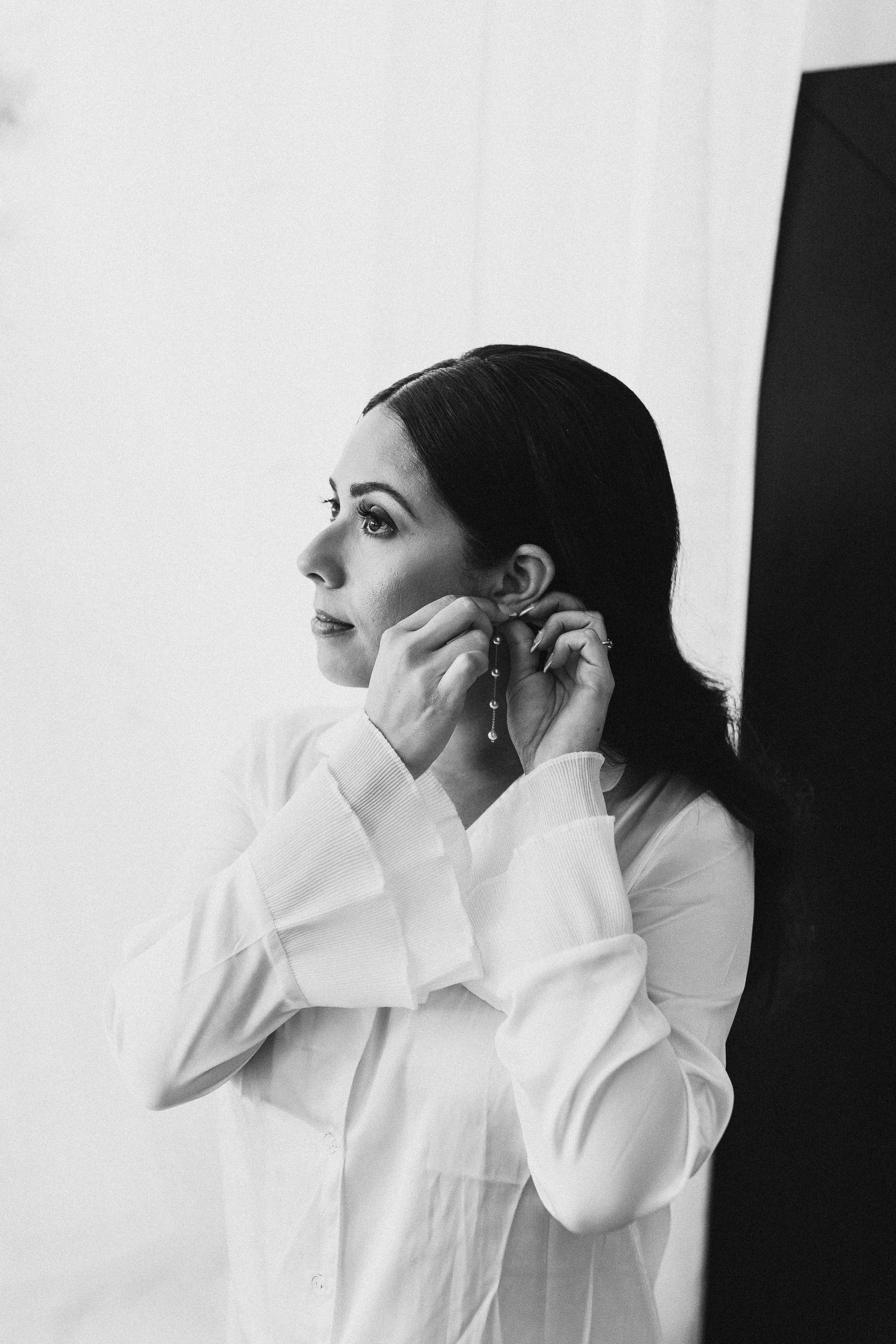 bride in white robe with bell sleeves putting on earrings