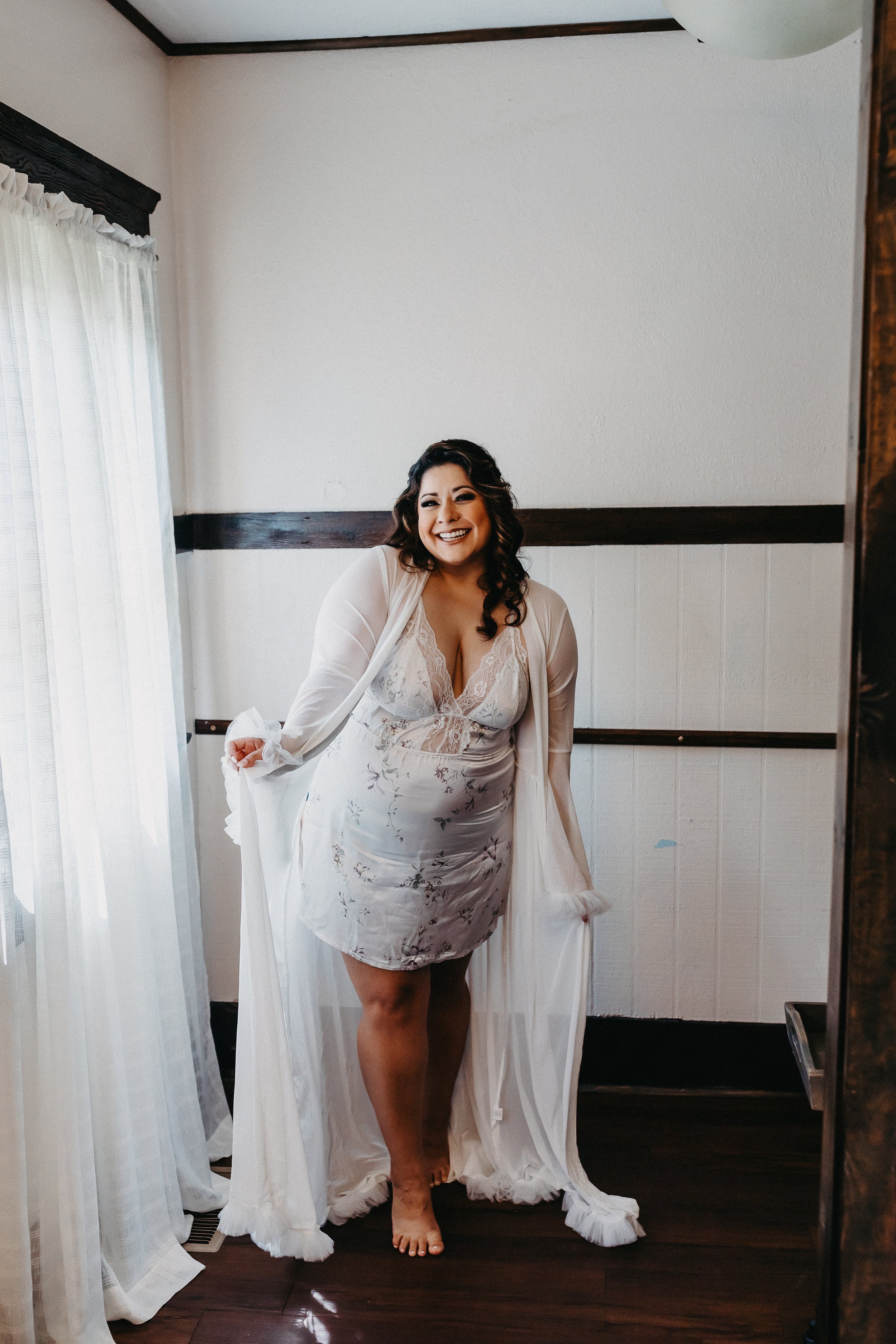 bride in floral and lace chemise with floor length white robe smiling at the camera