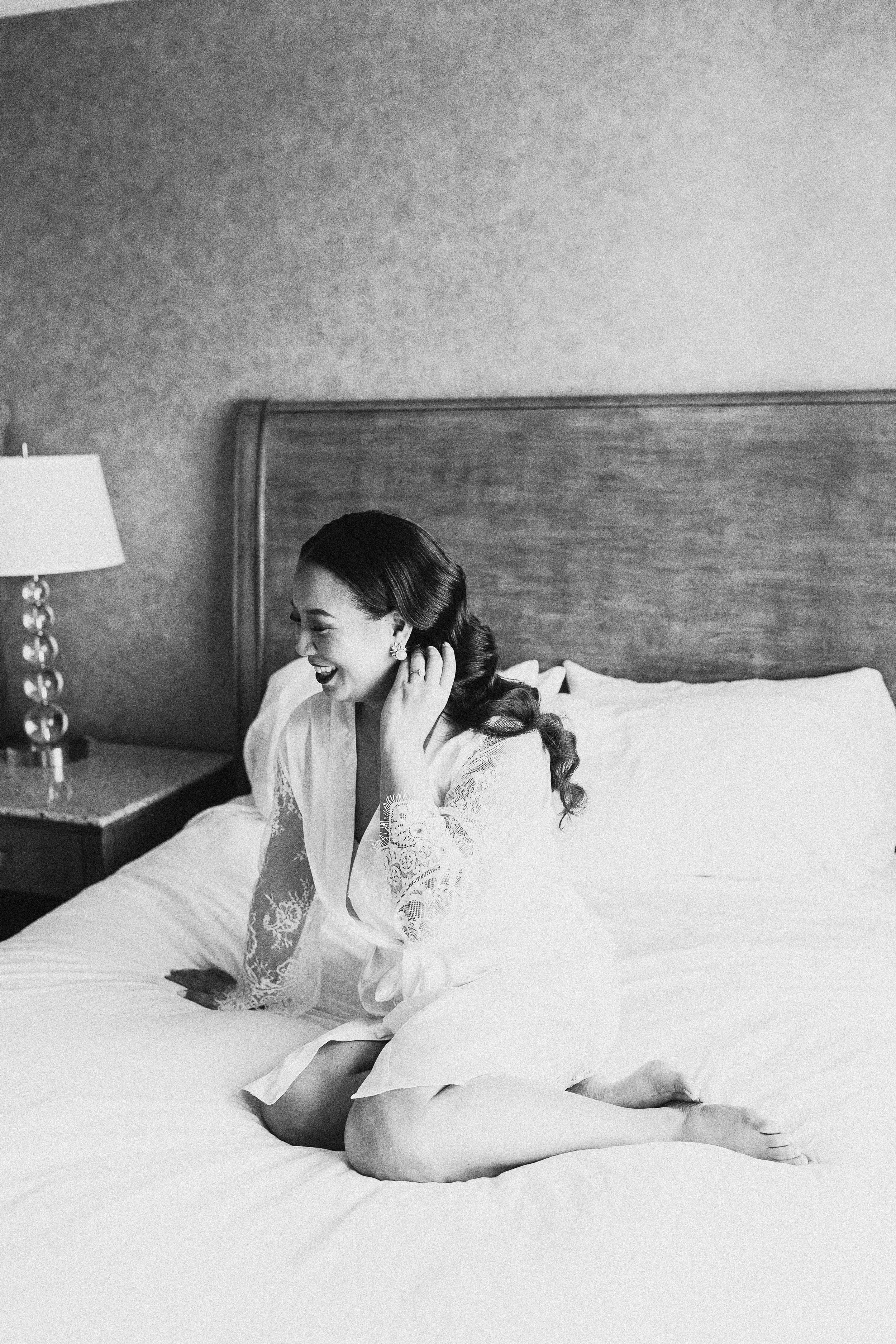 bride in white lace robe smiling on the bed
