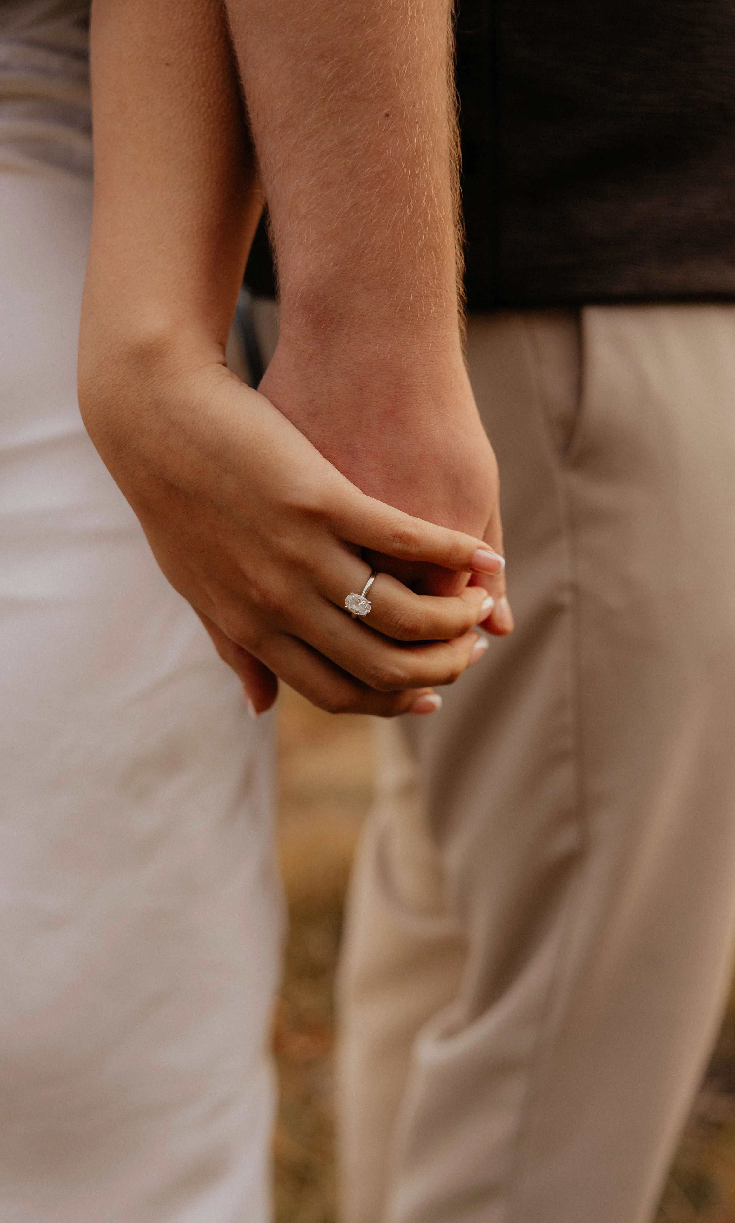 A woman wearing a diamond engagement ring, holding hands with a man, with their fingers intertwined.