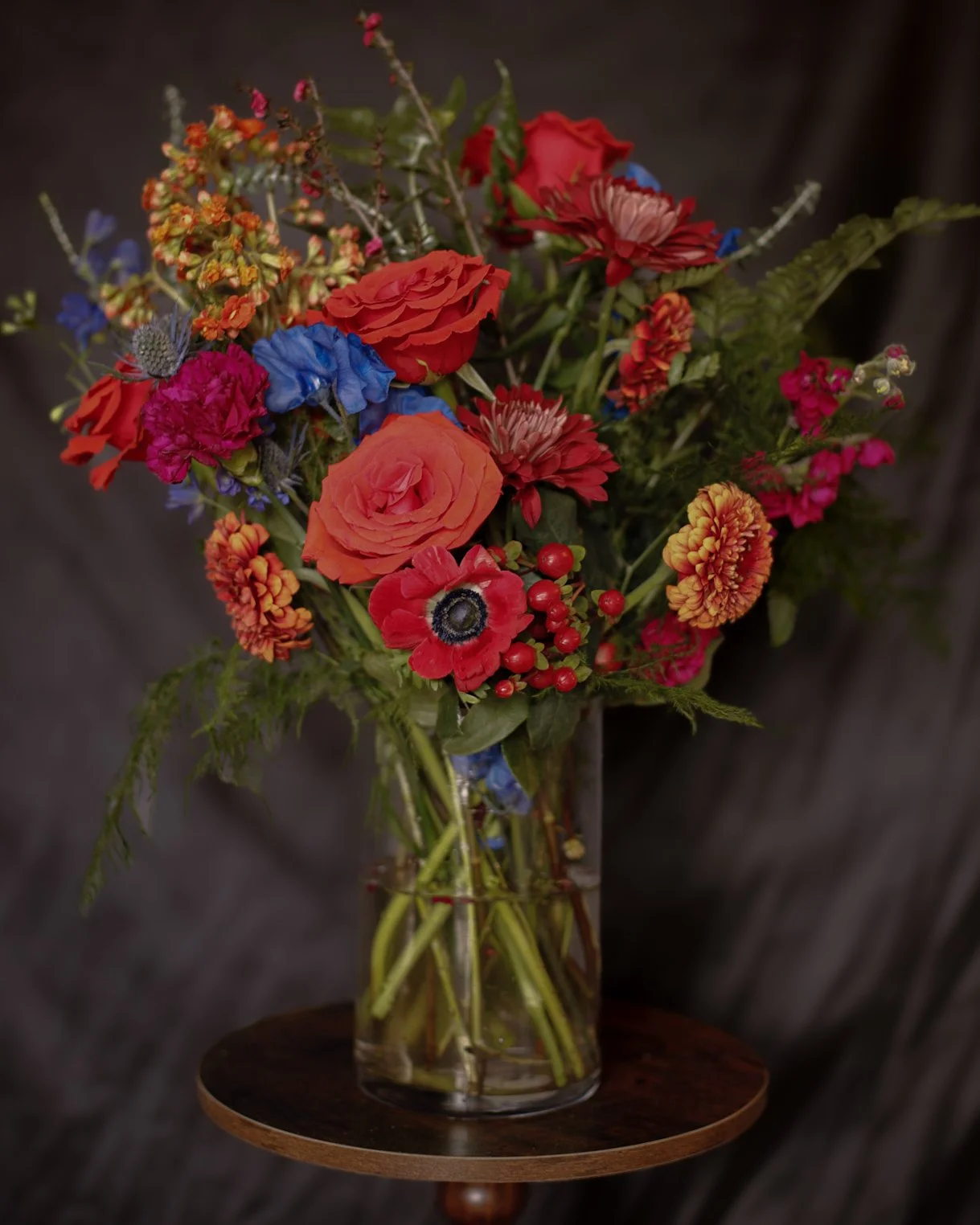 A bouquet of colorful flowers arranged in a clear glass vase on a small wooden table.